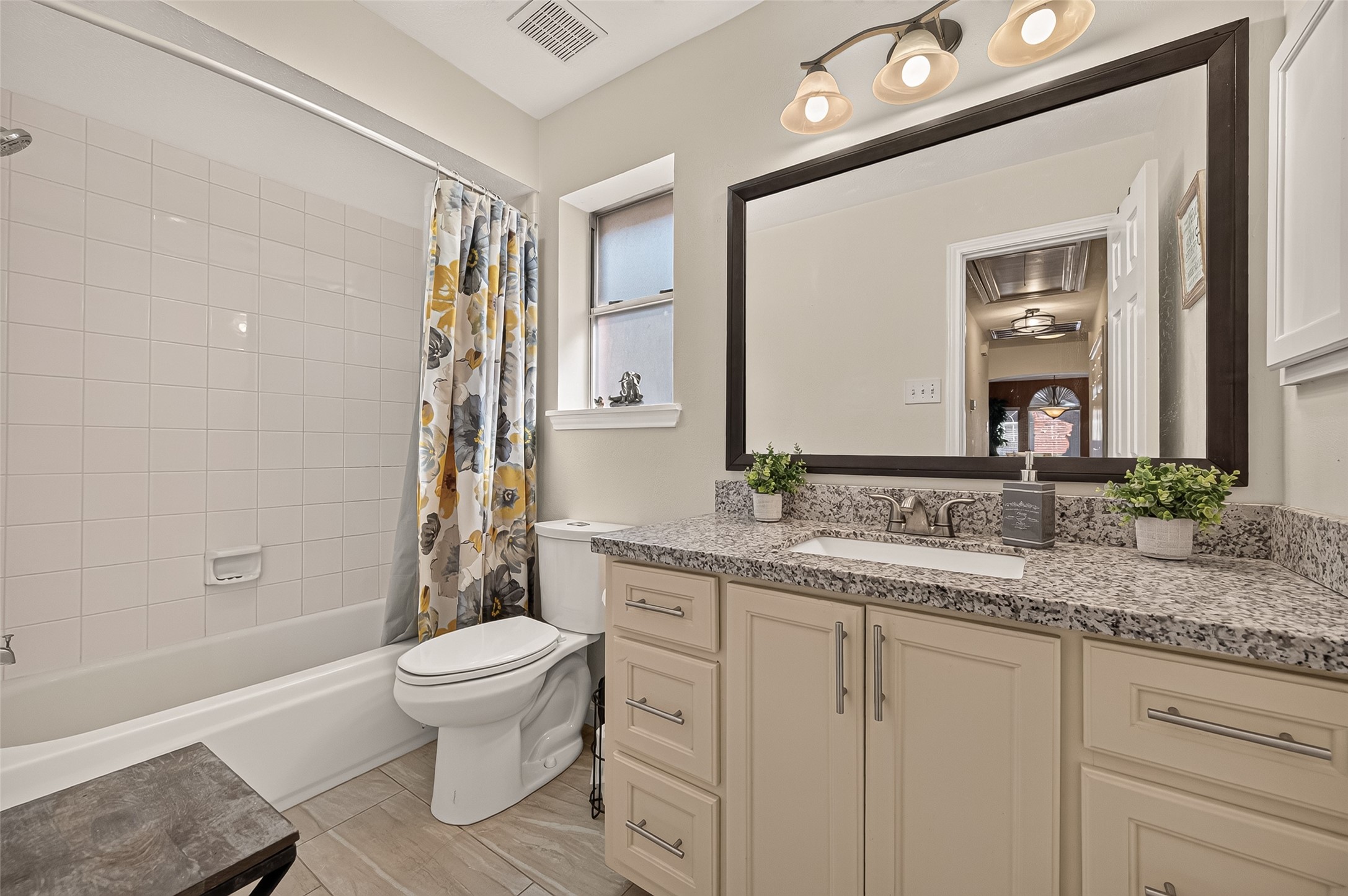 Charming bathroom with a modern granite-topped vanity, elegant lighting, and a classic tub-shower combo accented..