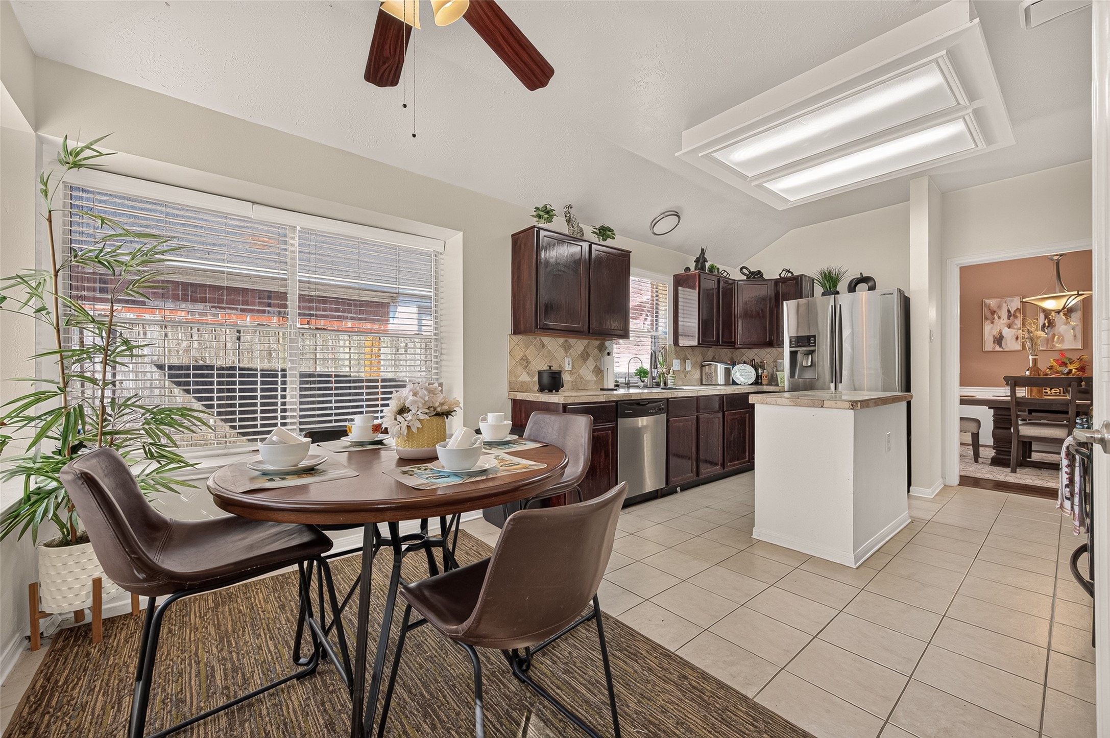 Bright kitchen with modern stainless steel appliances, dark wood cabinetry, and a cozy breakfast nook by a large window, offering a perfect space for casual dining.