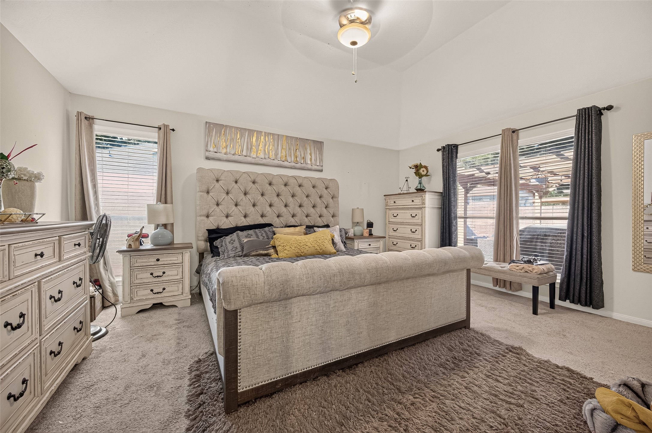 Spacious bedroom with a plush tufted bed, neutral tones, and ample natural light from large windows.