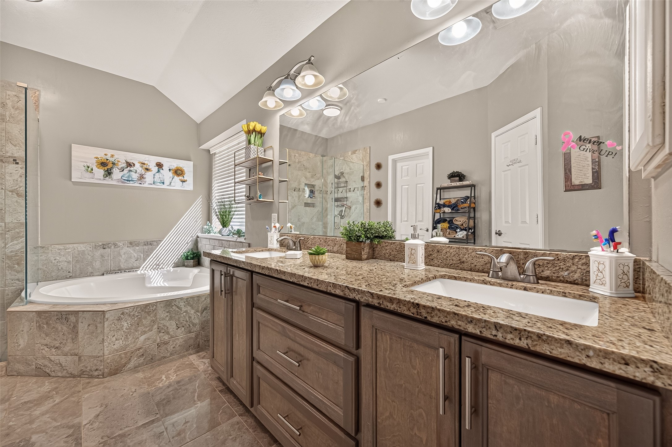 Spacious bathroom featuring a luxurious soaking tub, elegant granite countertops, dual sinks, and stylish wood cabinetry, complemented by tasteful decor and ample natural light.