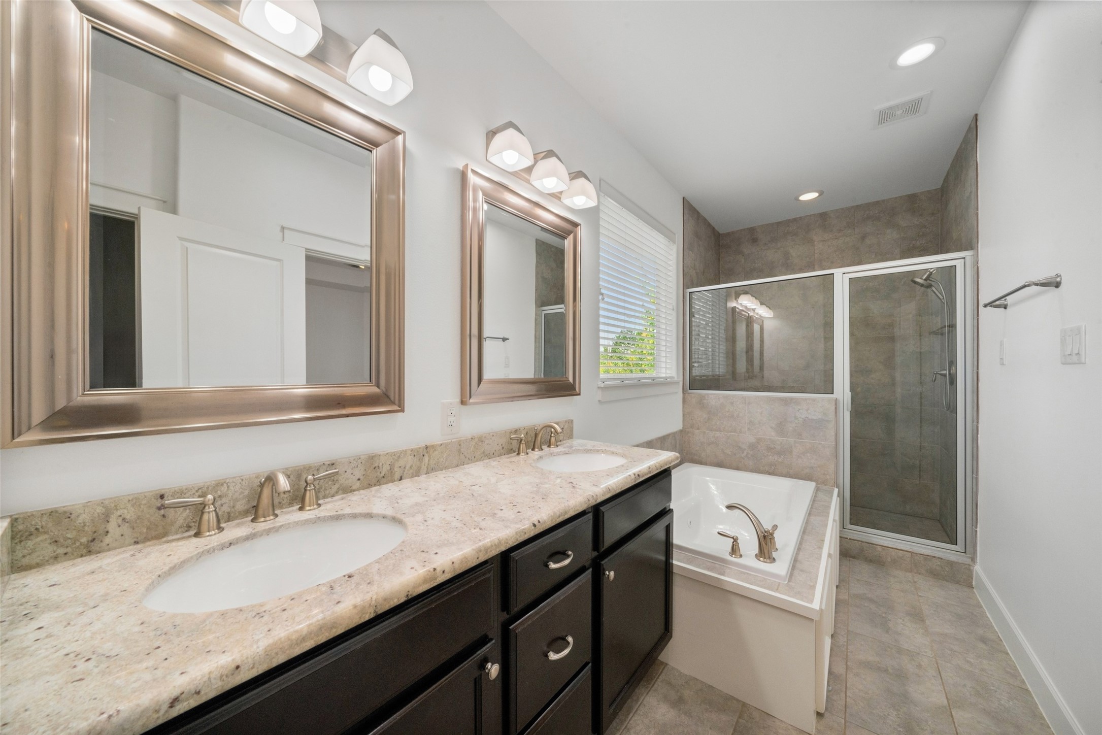 Your primary ensuite! This modern bathroom features dual sinks with a granite countertop, large mirrors, ample lighting, a glass-enclosed shower, and a separate jetted tub.