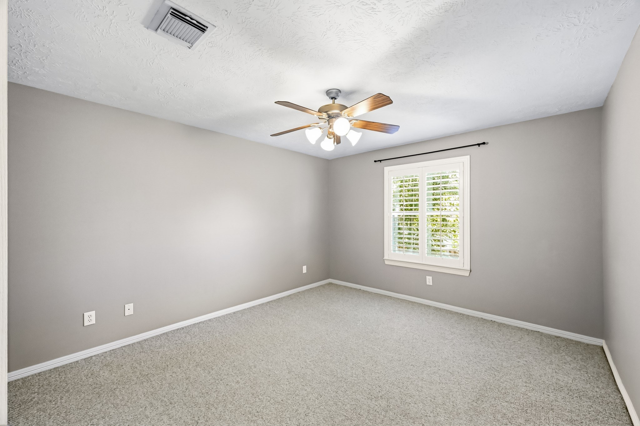 Bright secondary bedroom with Berber carpet, ceiling fan, and plantation shutters.