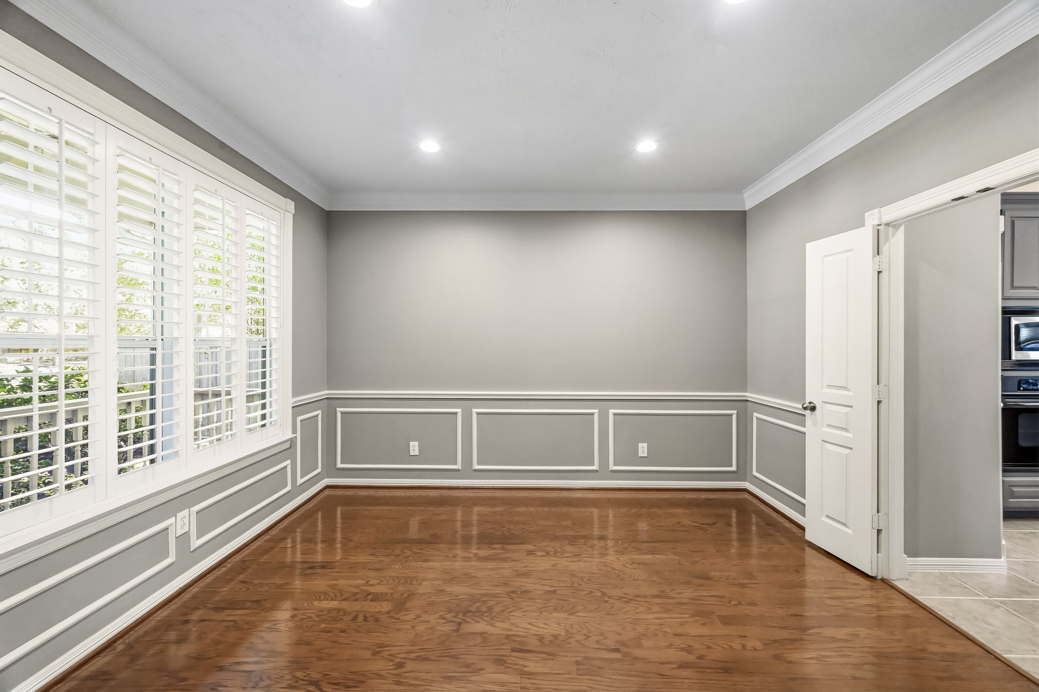 Elegant formal dining room featuring hardwood floors, decorative wall molding, crown molding, and plantation shutters. Conveniently located right off the kitchen.