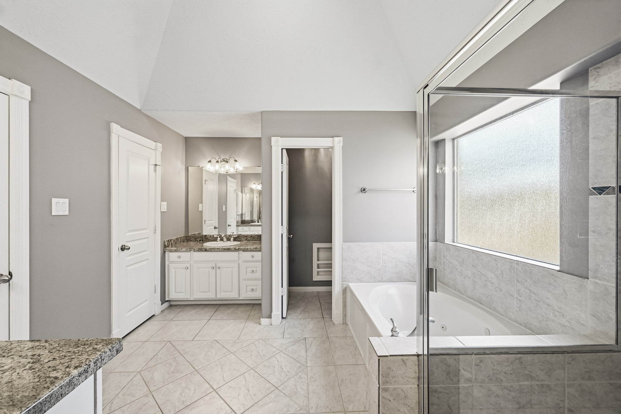 Spacious primary bathroom with granite countertops, tile flooring, a separate soaking tub, and a glass-enclosed shower.