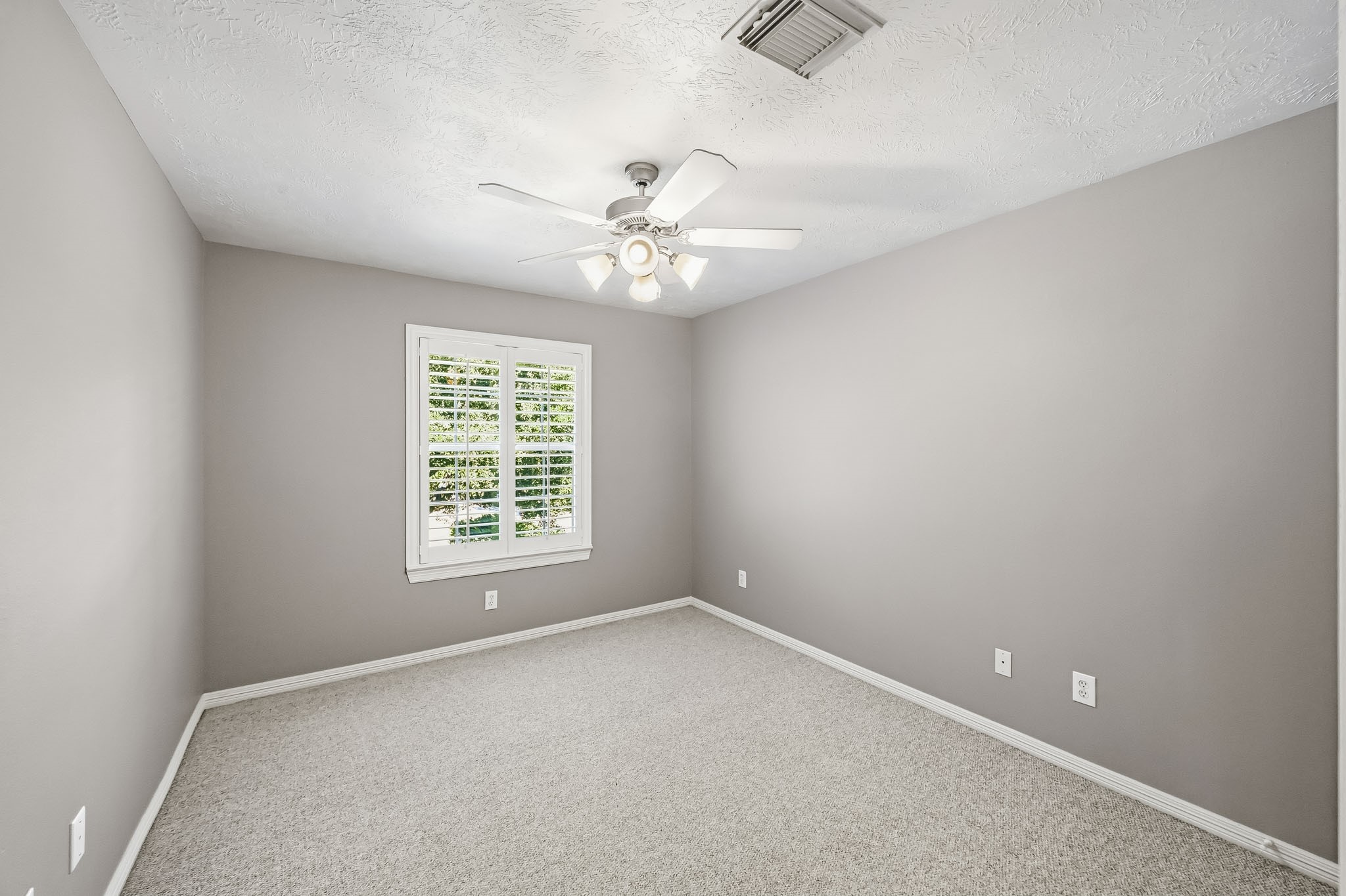 Another secondary bedroom offering neutral finishes, Berber carpet, ceiling fan, and plantation shutters.