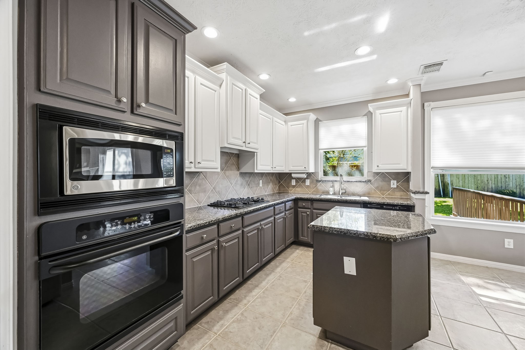 Spacious kitchen with granite countertops, center island, abundant cabinetry, tile backsplash, and built-in appliances.