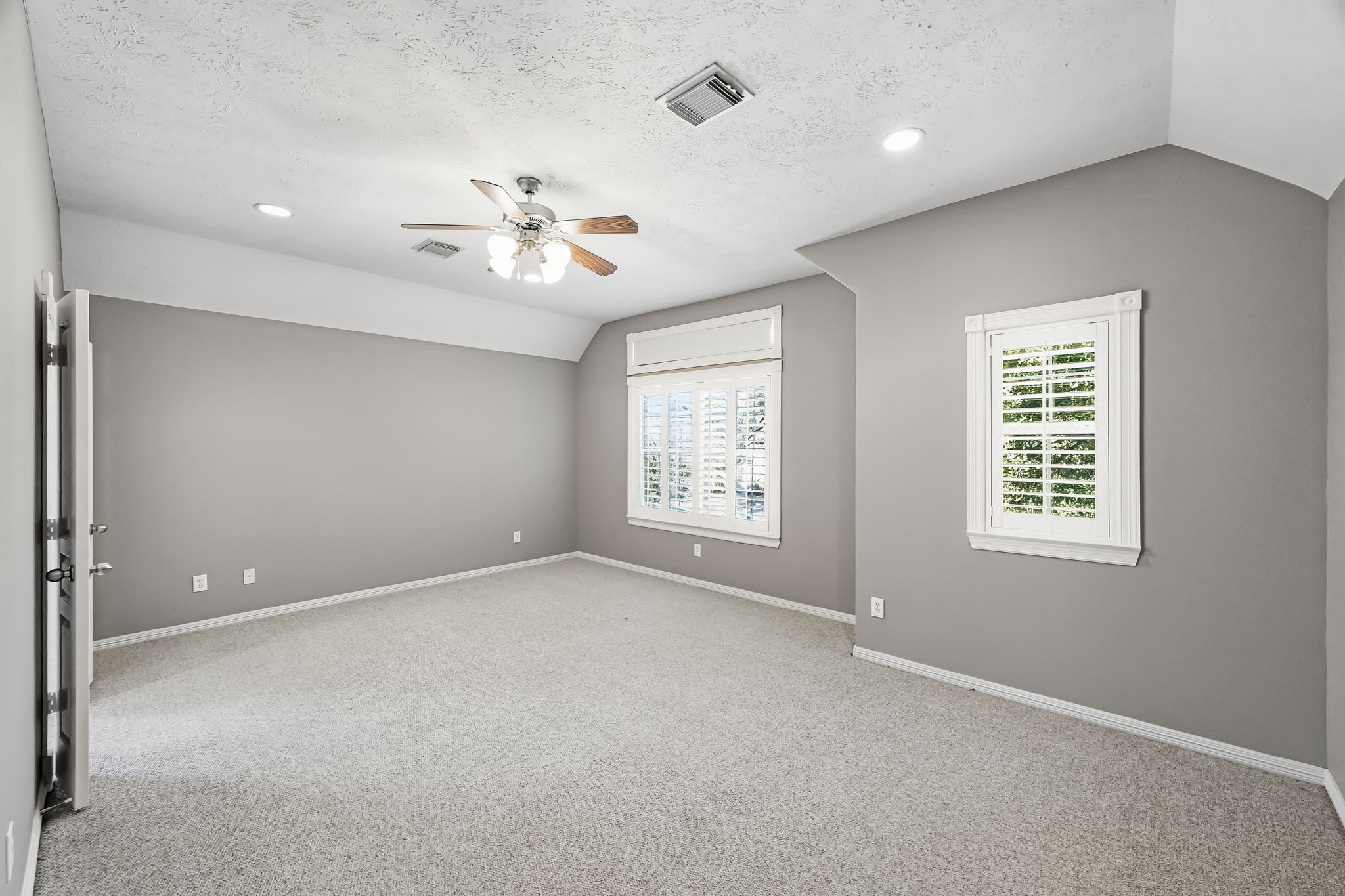 Generously sized primary suite featuring Berber carpet, a ceiling fan, abundant natural light, and plantation shutters.