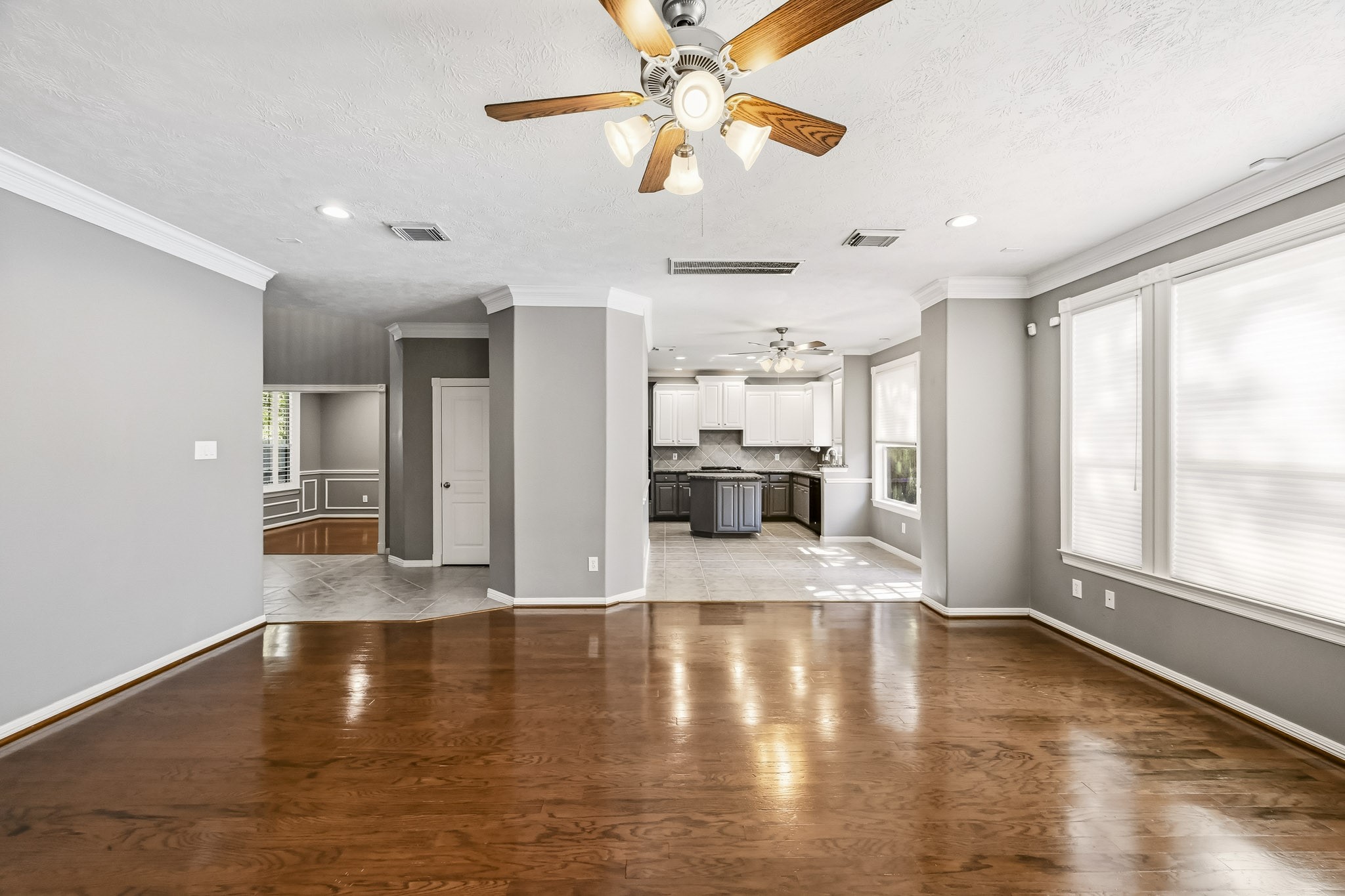 Spacious family room with hardwood floors, crown molding, and ceiling fan. Open layout connects the living space to the kitchen and breakfast area.
