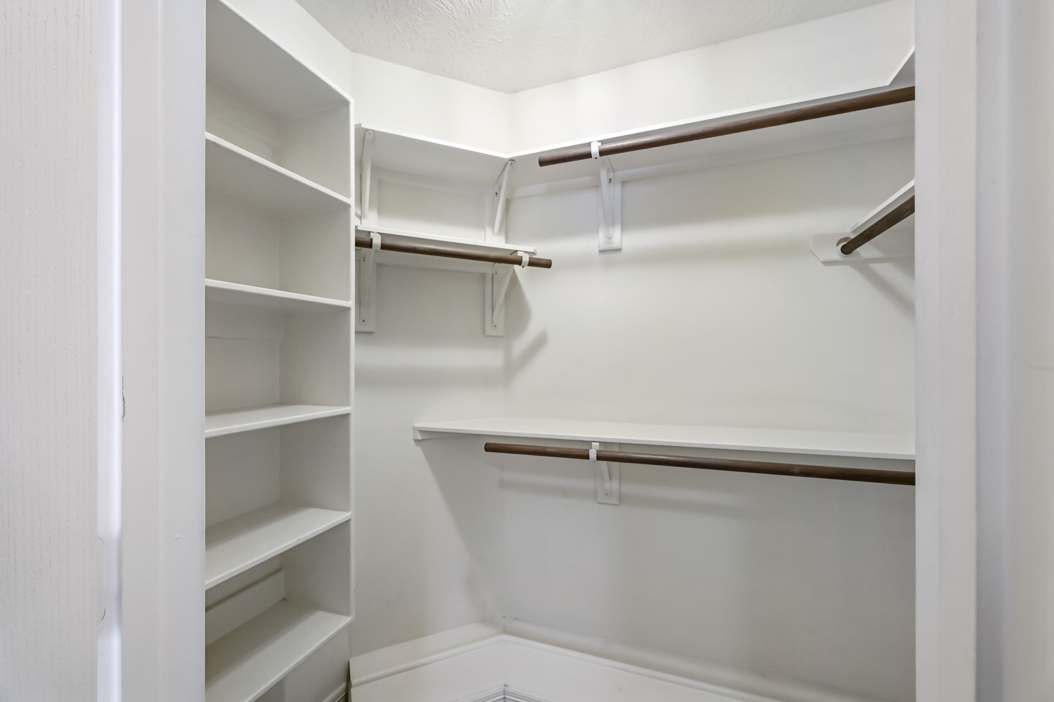 Spacious walk-in primary closet featuring built-in shelving, multiple hanging rods, and plenty of storage to keep everything organized.