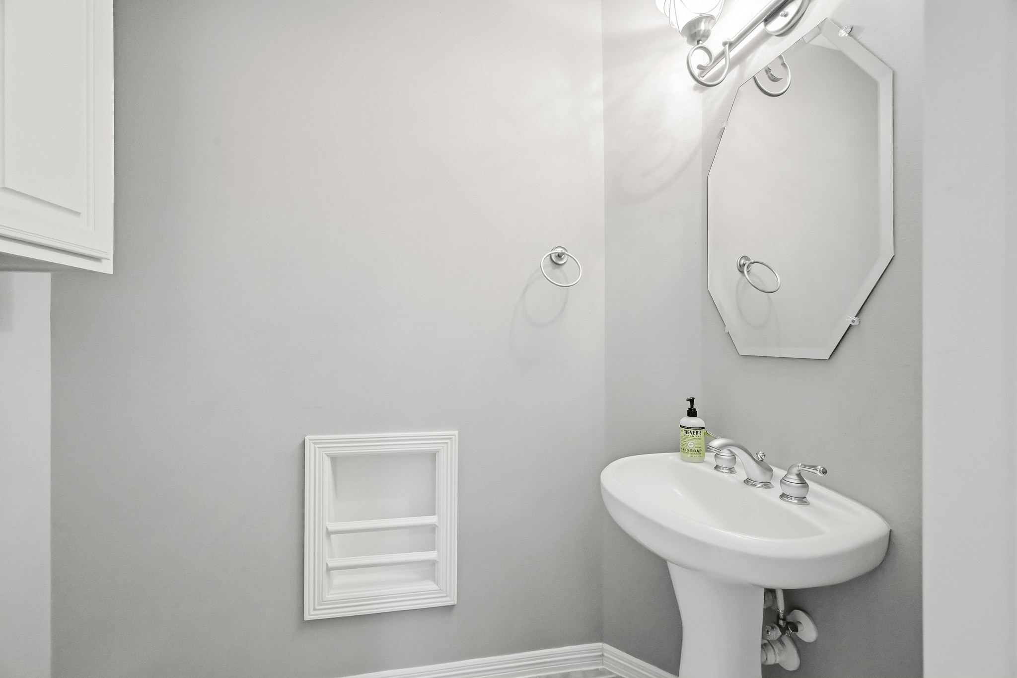 Convenient downstairs powder room featuring a pedestal sink, decorative mirror, and neutral finishes.
