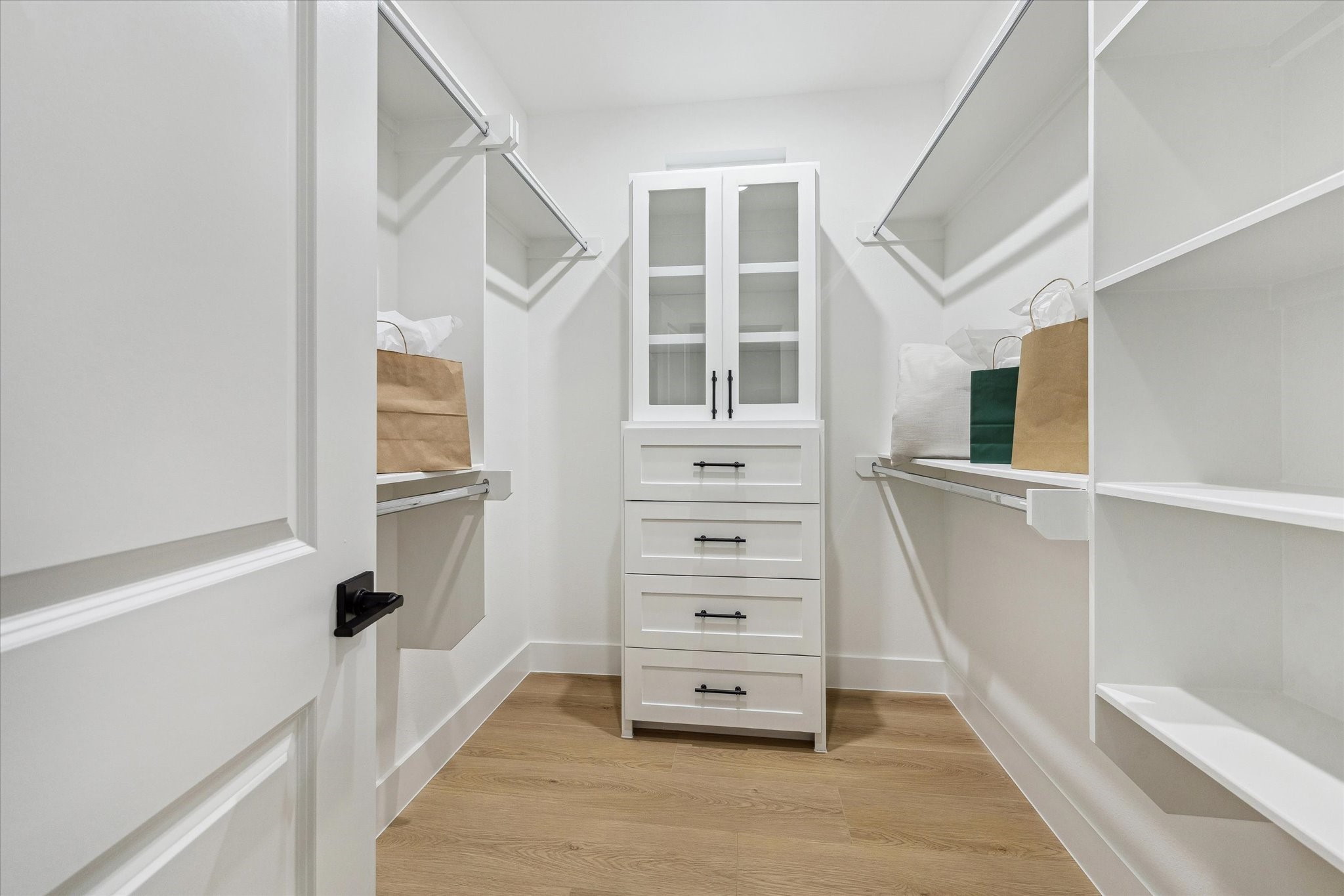 Spacious walk-in closet featuring built-in shelving, ample hanging space, and a central cabinet with drawers for organized storage.
