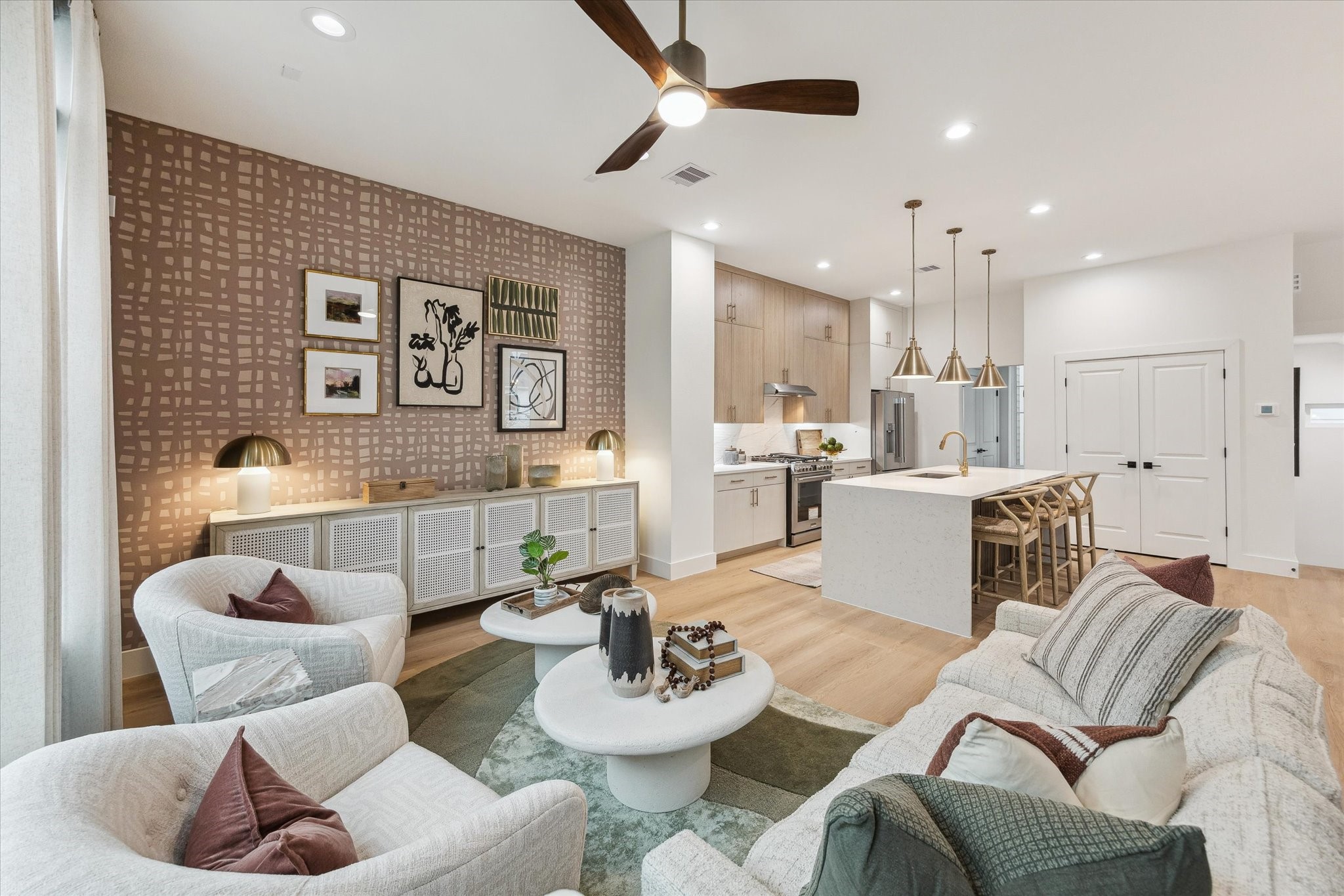 Experience modern elegance in this open-concept living space, featuring a stylish kitchen with an island, sleek cabinetry, and pendant lighting. The cozy sitting area is enhanced by a chic accent wall and contemporary decor, creating a perfect blend of comfort and sophistication.