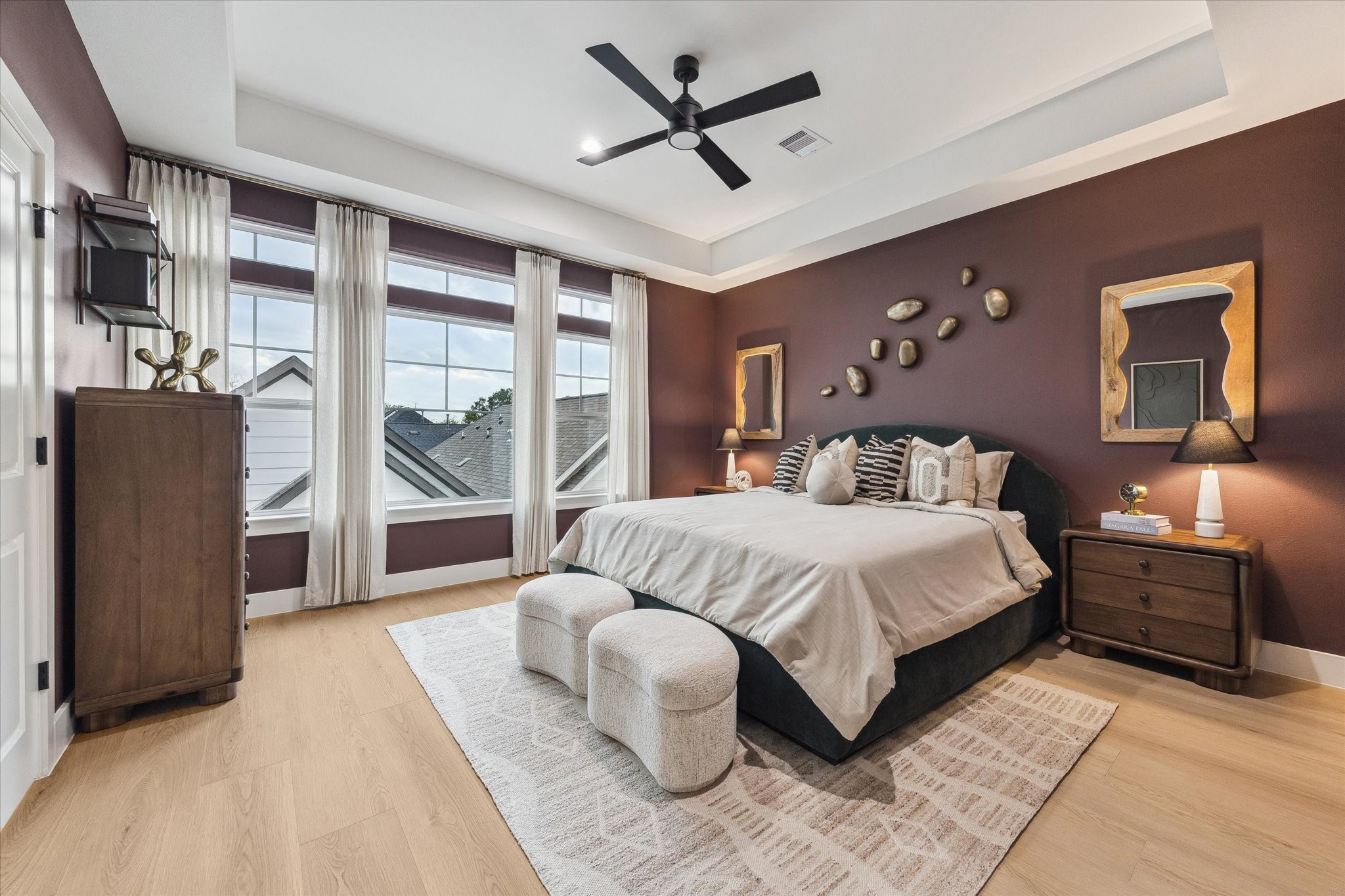 Spacious bedroom with a luxurious king-sized bed, large windows offering ample natural light, elegant decor, and rich, warm tones for a cozy atmosphere.