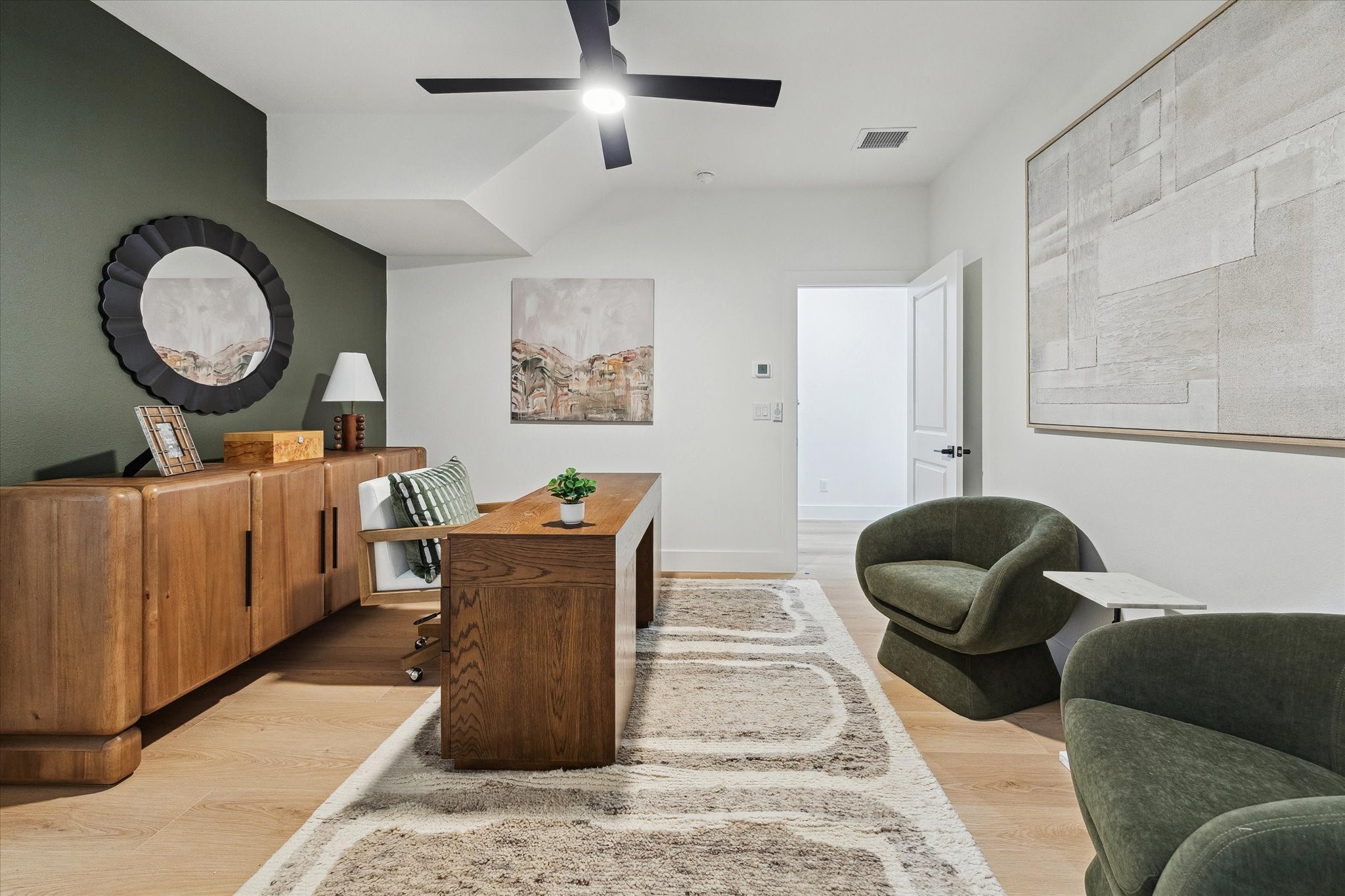 Elegant home office with a modern wooden desk, plush seating, and stylish decor, complemented by a sleek ceiling fan and natural light.