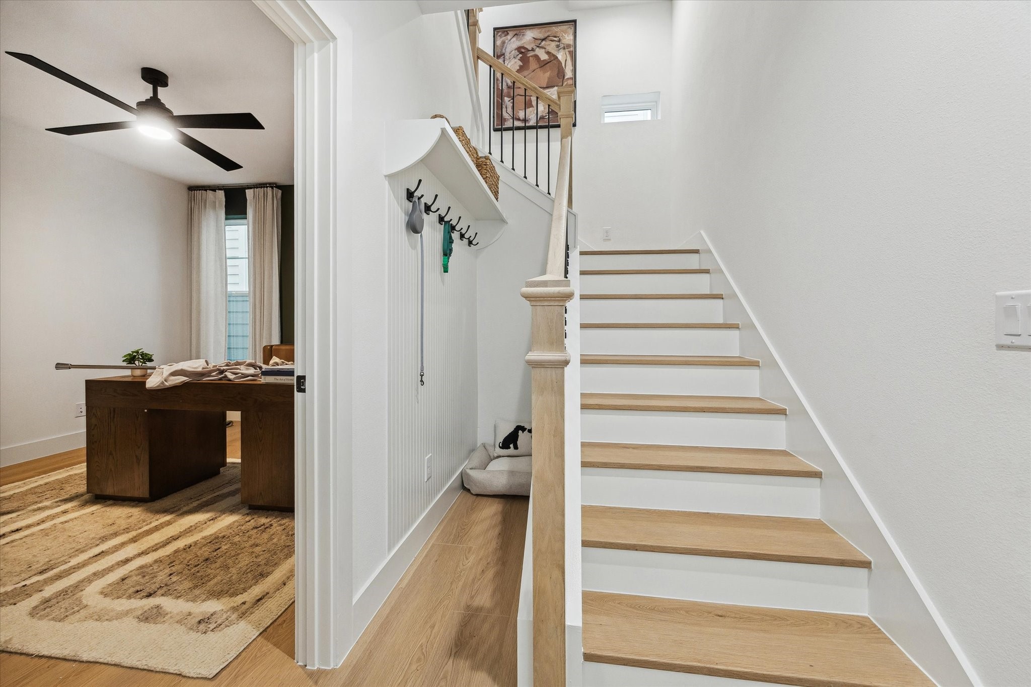 Bright and inviting entryway featuring sleek wooden stairs and a modern office space with a ceiling fan, perfect for work-from-home needs.