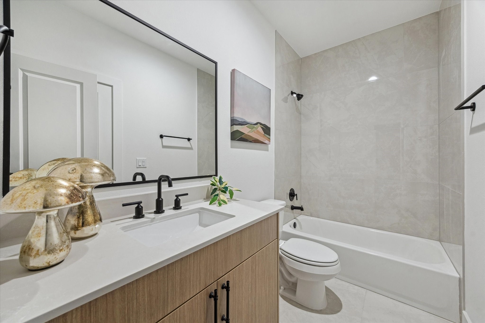 Sleek modern bathroom featuring a spacious vanity with dual faucets, a large mirror, and elegant fixtures. The tiled bathtub area adds a touch of luxury, complemented by tasteful decorative accents.
