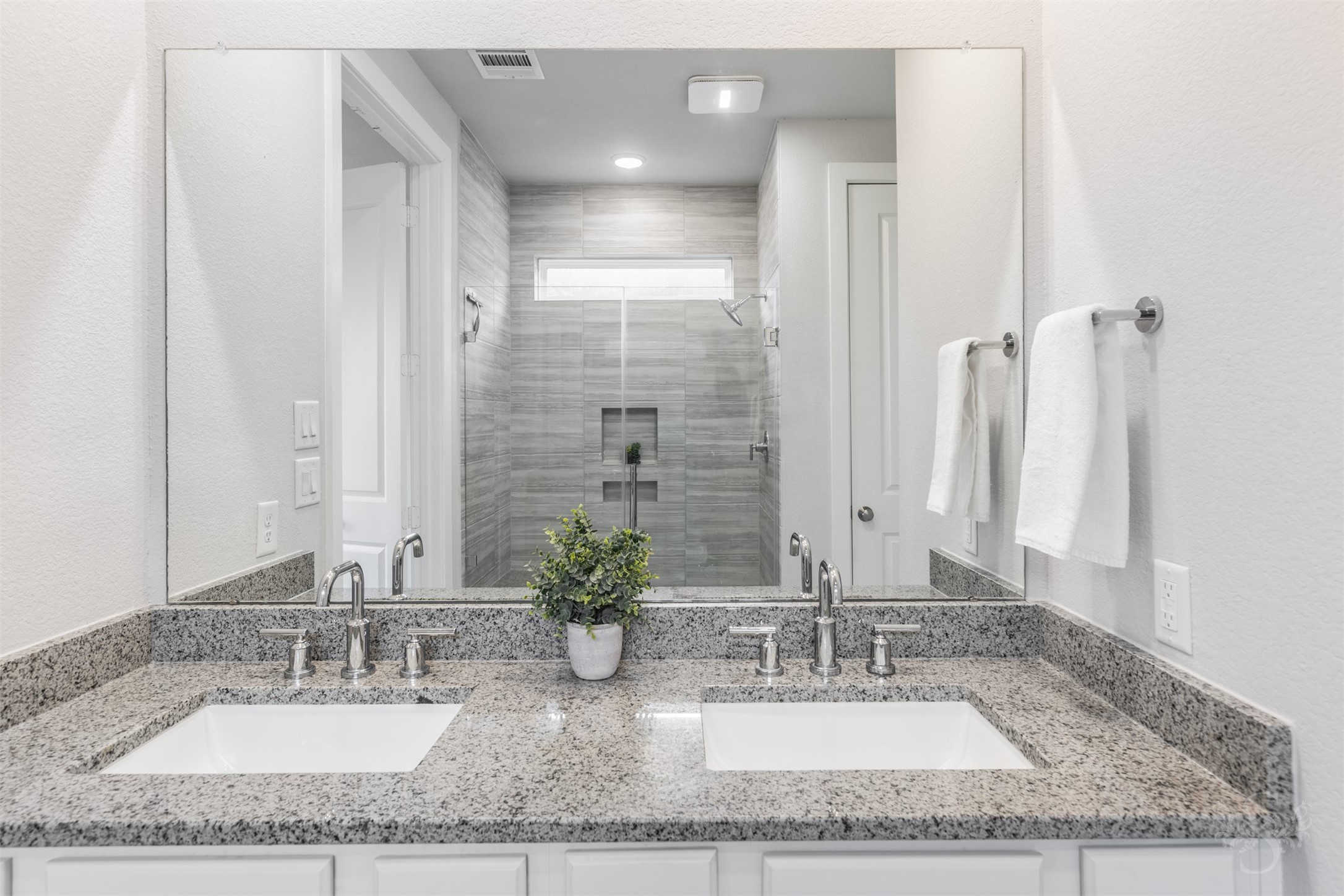Dual undermount sinks and polished chrome fixtures complement the primary baths gorgeous granite vanity. An expansive mirror stretches above the counter, while cabinetry below keeps everyday essentials neatly tucked away.