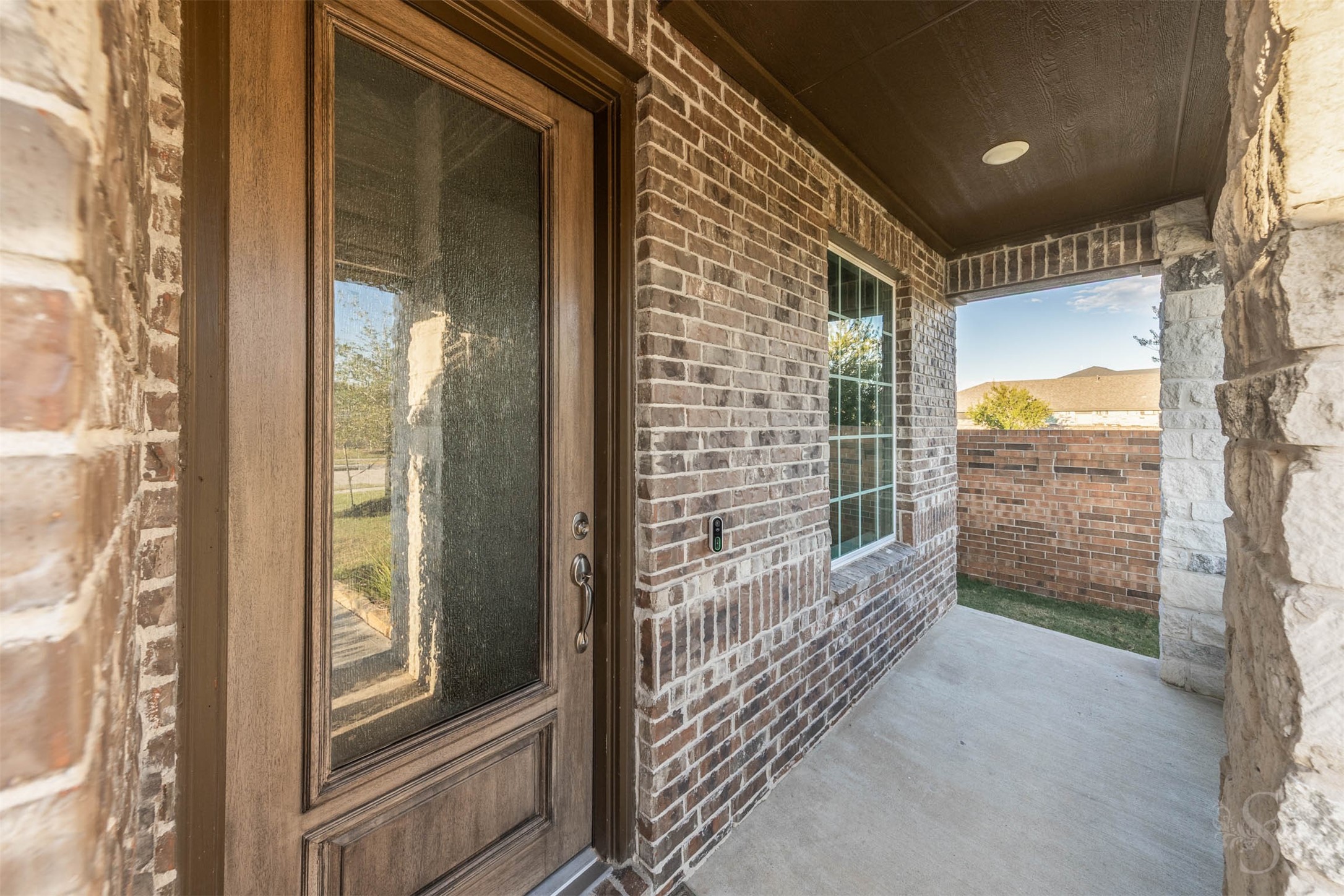 Rich brickwork and stone accents frame the sheltered front porch, creating a beautiful welcome to this stylish Taylor Morrison home. A wood front door with textured glass offers an elegant introduction to the inviting spaces within.