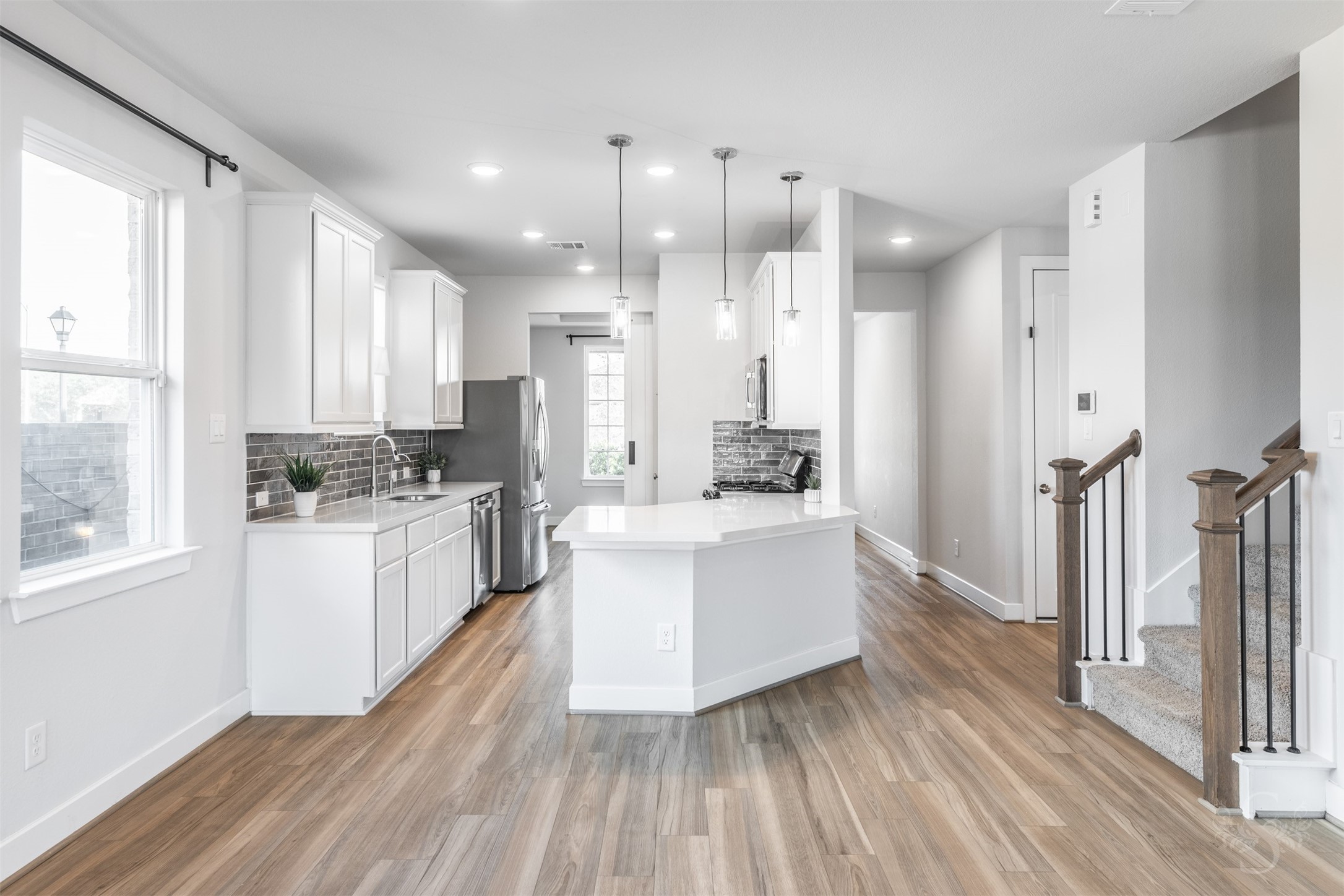Exquisite white quartz counters, crisp white cabinetry and a rich tile backsplash create a stylish kitchen complemented by stainless steel appliances and gorgeous wood flooring. A generous island beneath three pendant lights offers the perfect place to gather while meals are prepared.