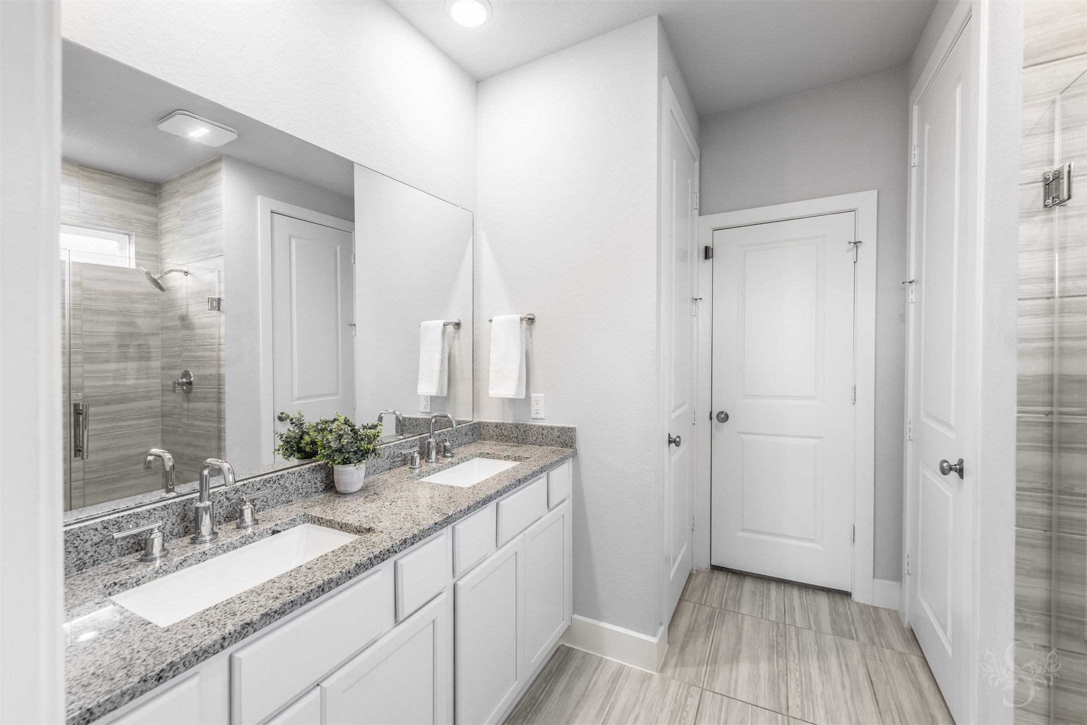 The beautiful primary bath features an extended vanity with dual sinks, granite counters and crisp white cabinetry. Coordinating tile flooring and a spacious glass-enclosed shower create an elegant setting for your daily routine.