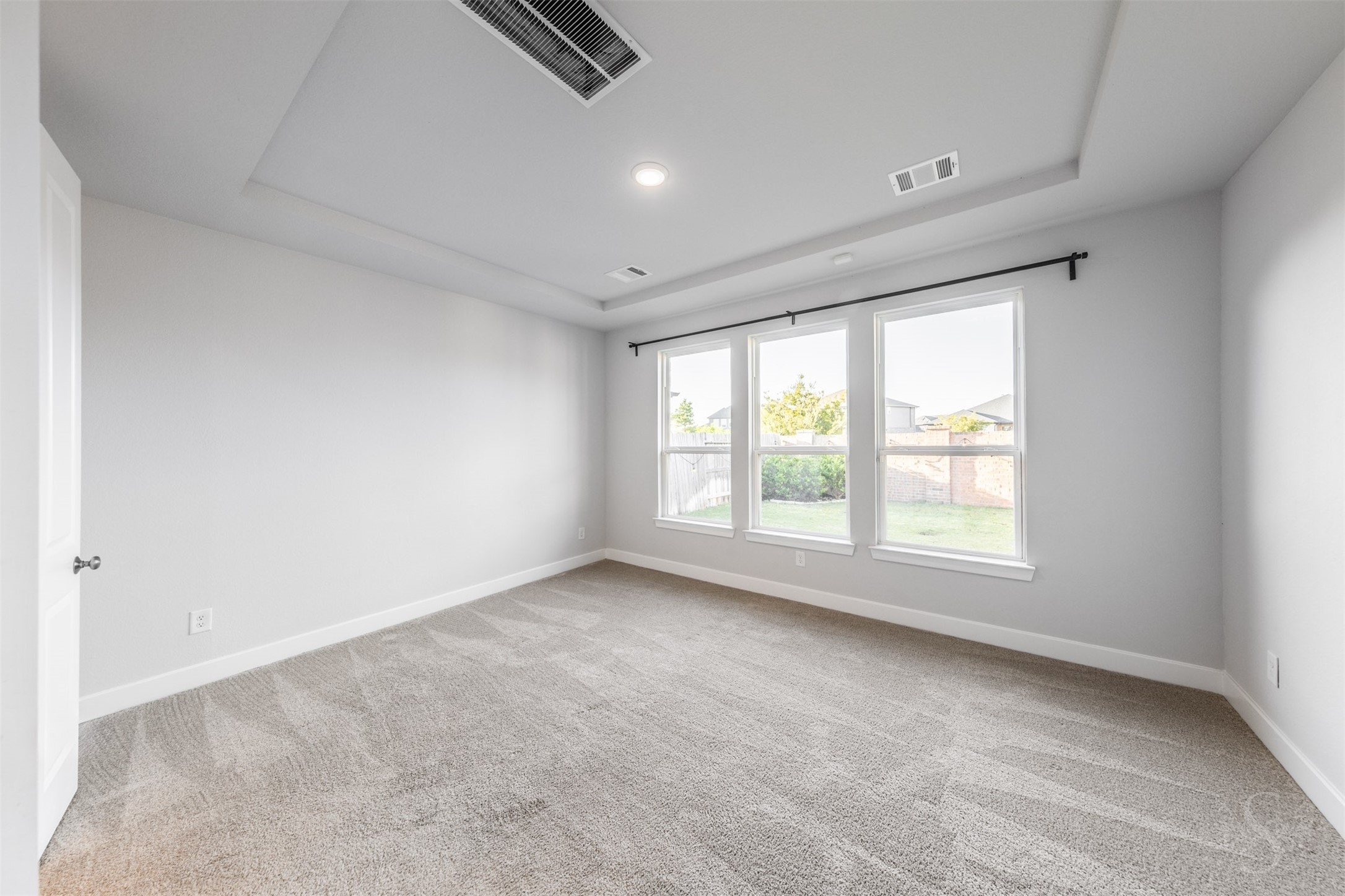 The spacious primary bedroom offers a peaceful retreat with an elegant tray ceiling and soft, neutral finishes. Three large windows overlook the back yard, creating a bright and inviting place to unwind.