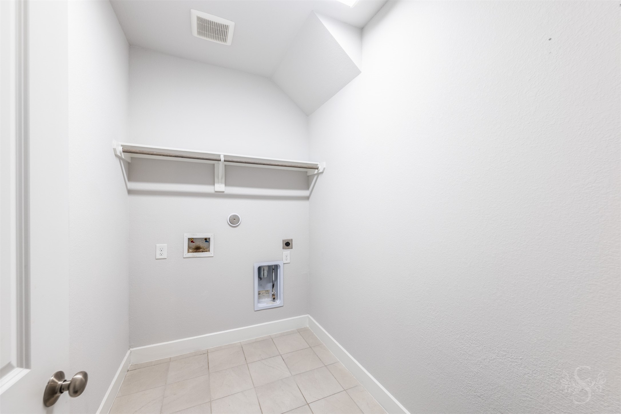 The laundry room features tile flooring and a convenient overhead shelf for storing everyday essentials. A hanging rod provides a handy spot to air-dry clothing or hang freshly pressed items.
