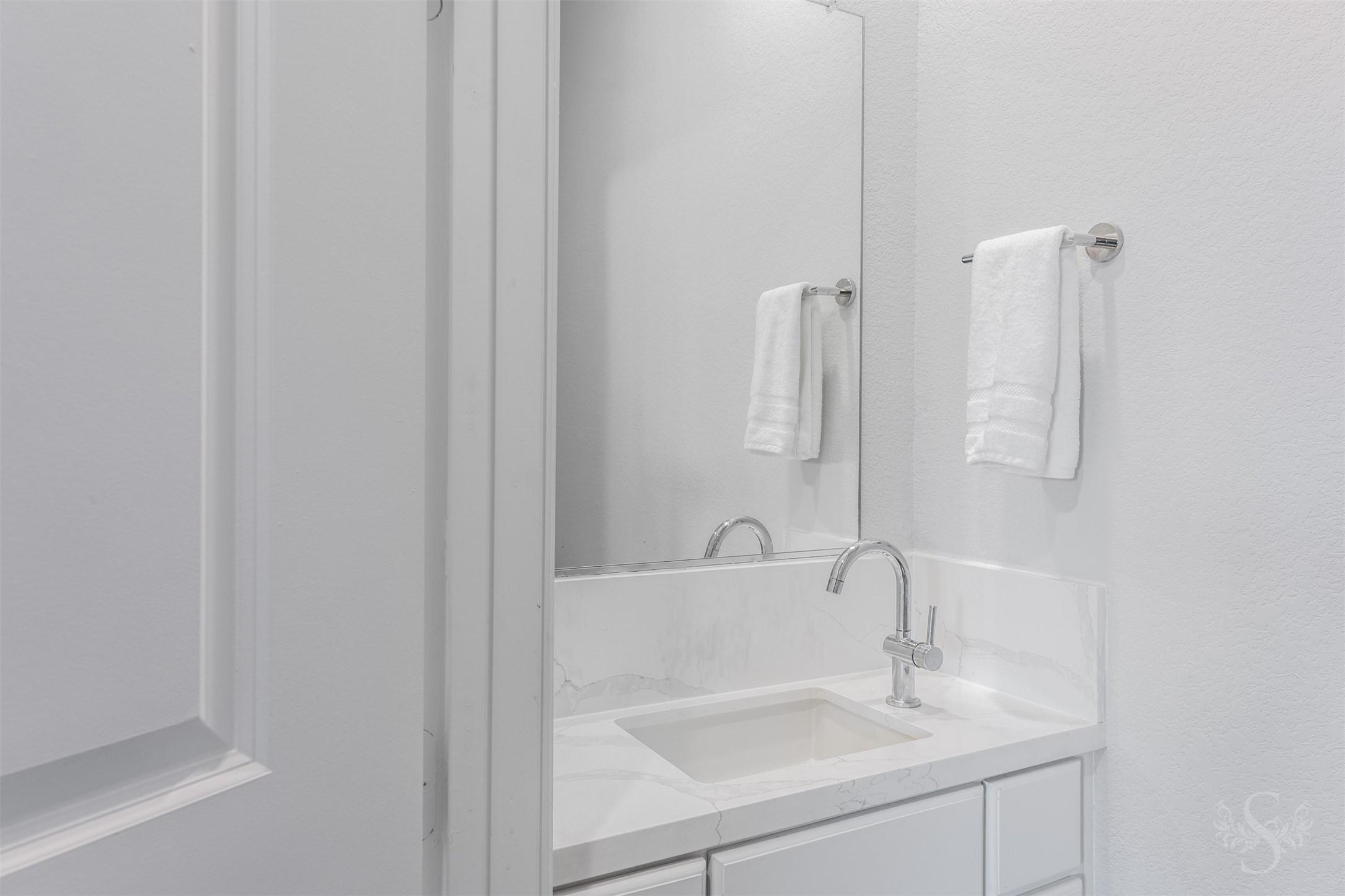 This stylish bath features a beautiful countertop and backsplash paired with crisp white cabinetry. A sleek chrome faucet and large mirror complete the bright, polished space.