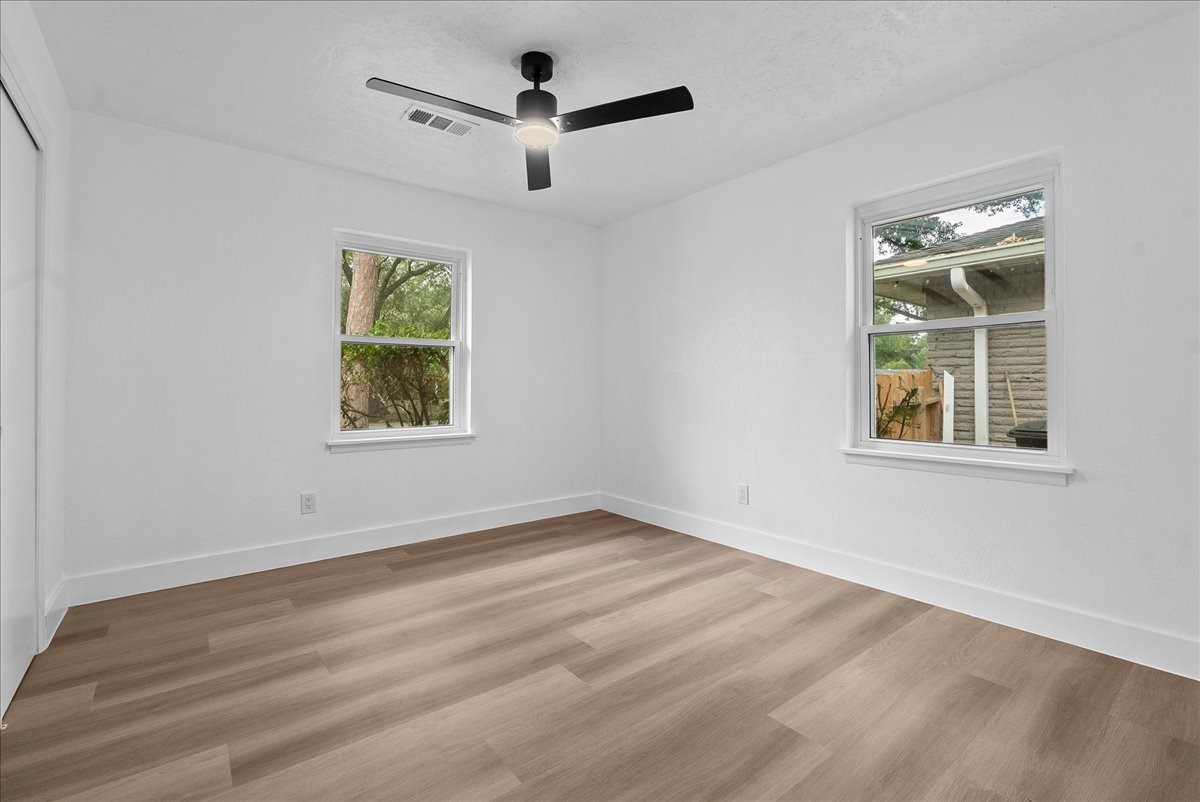 Bright and inviting room with natural light, featuring sleek wood flooring and a modern ceiling fan.