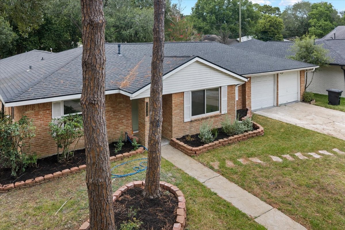 Charming brick home with a spacious two-car garage, surrounded by lush greenery and a well-maintained garden.