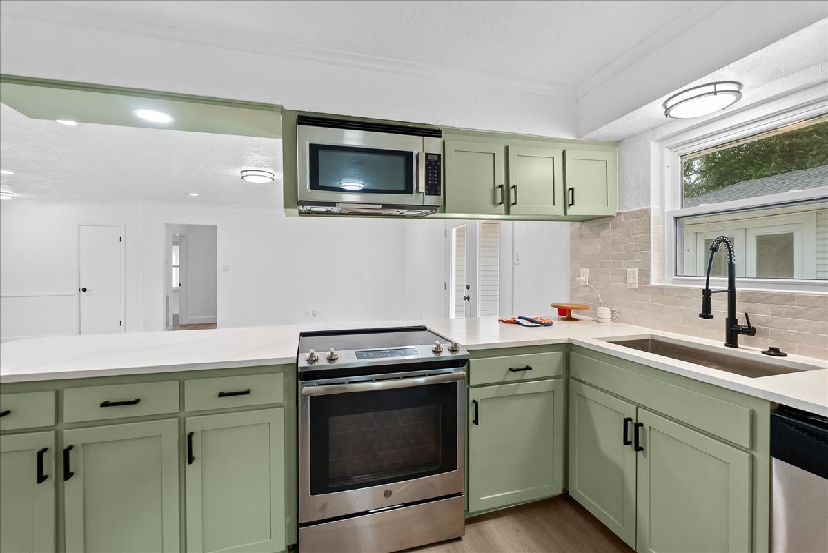 Modern kitchen featuring sleek appliances, soft green cabinetry, and ample counter space, all bathed in natural light from a large window.