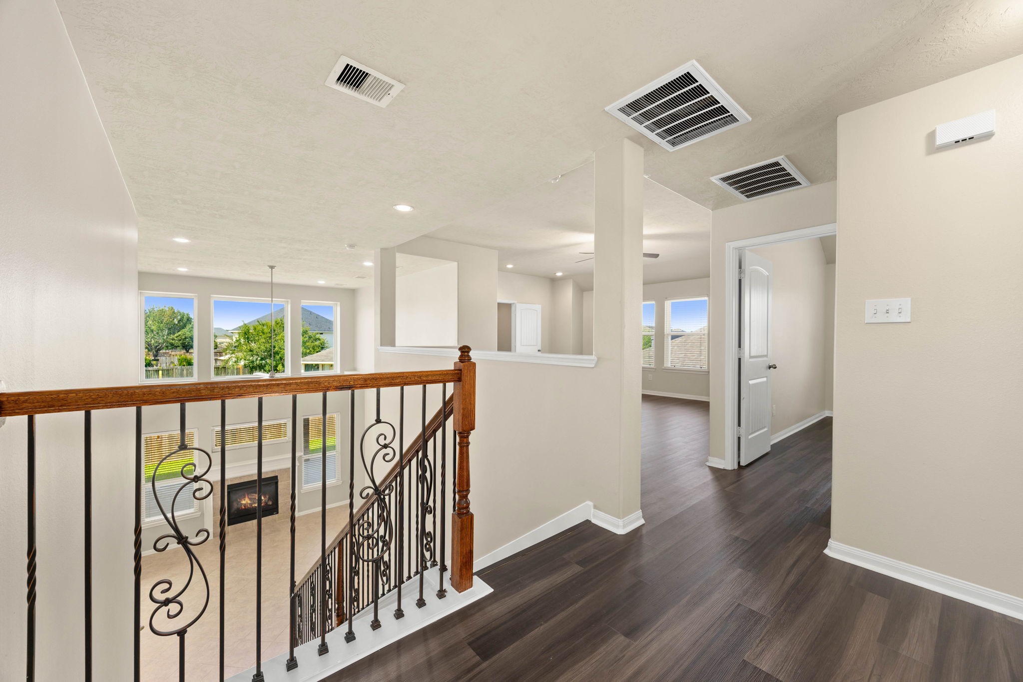 Come upstairs to a spacious landing that seamlessly connects the home's second-level retreat. Rich dark wood flooring spans this open corridor, which features an elegant wrought-iron railing overlooking the family room below, while offering a clear view into the adjacent, sunlit game room and the hallway leading to the private secondary bedrooms.