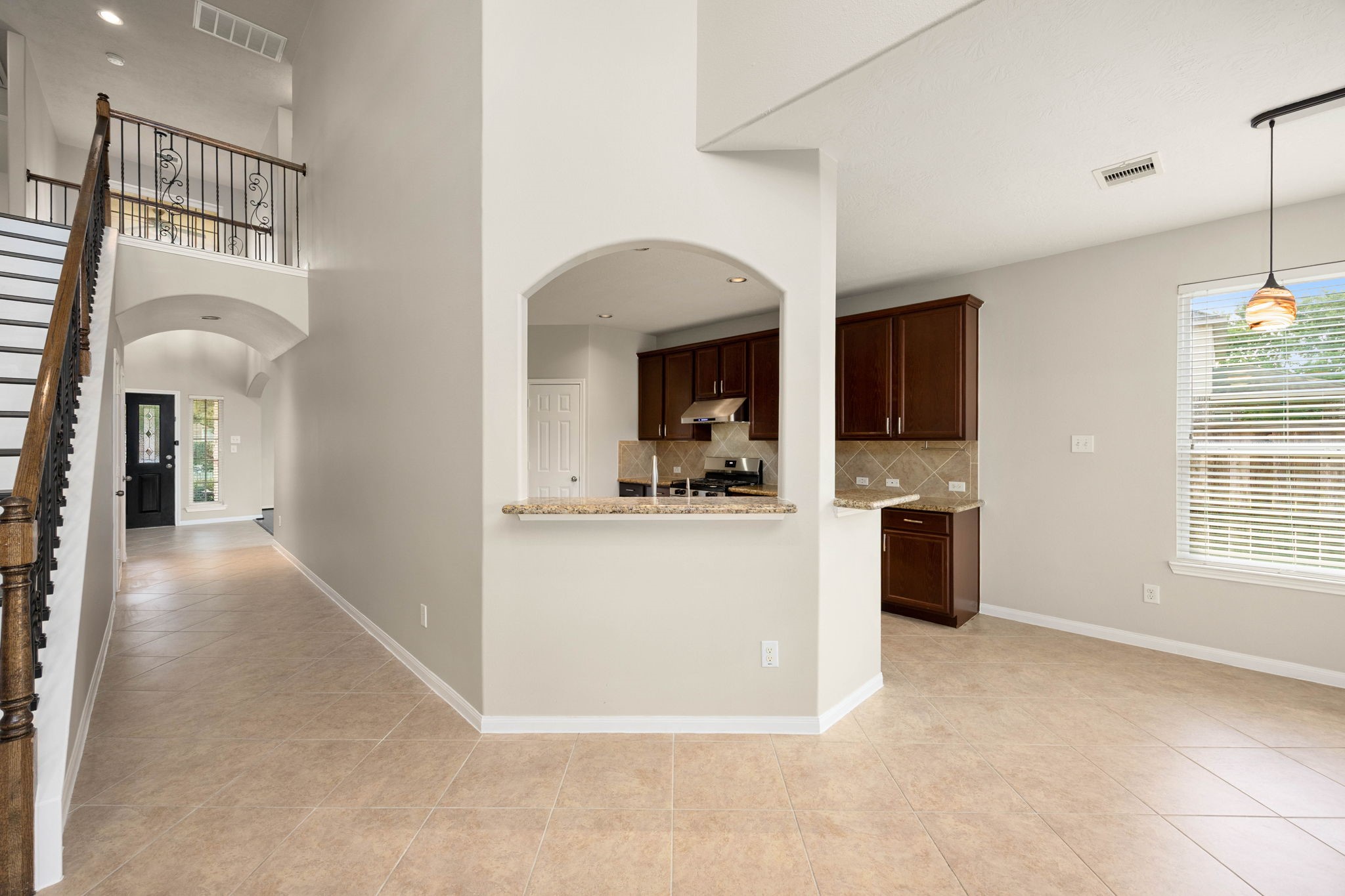 An elegant arched pass-through window creates a seamless visual connection between the kitchen and the central family room, keeping the home feeling bright and integrated. This unique architectural detail frames the rich dark cabinetry, granite countertops, and tiled backsplash of the kitchen while preserving the distinct spaces of the main floor layout.
