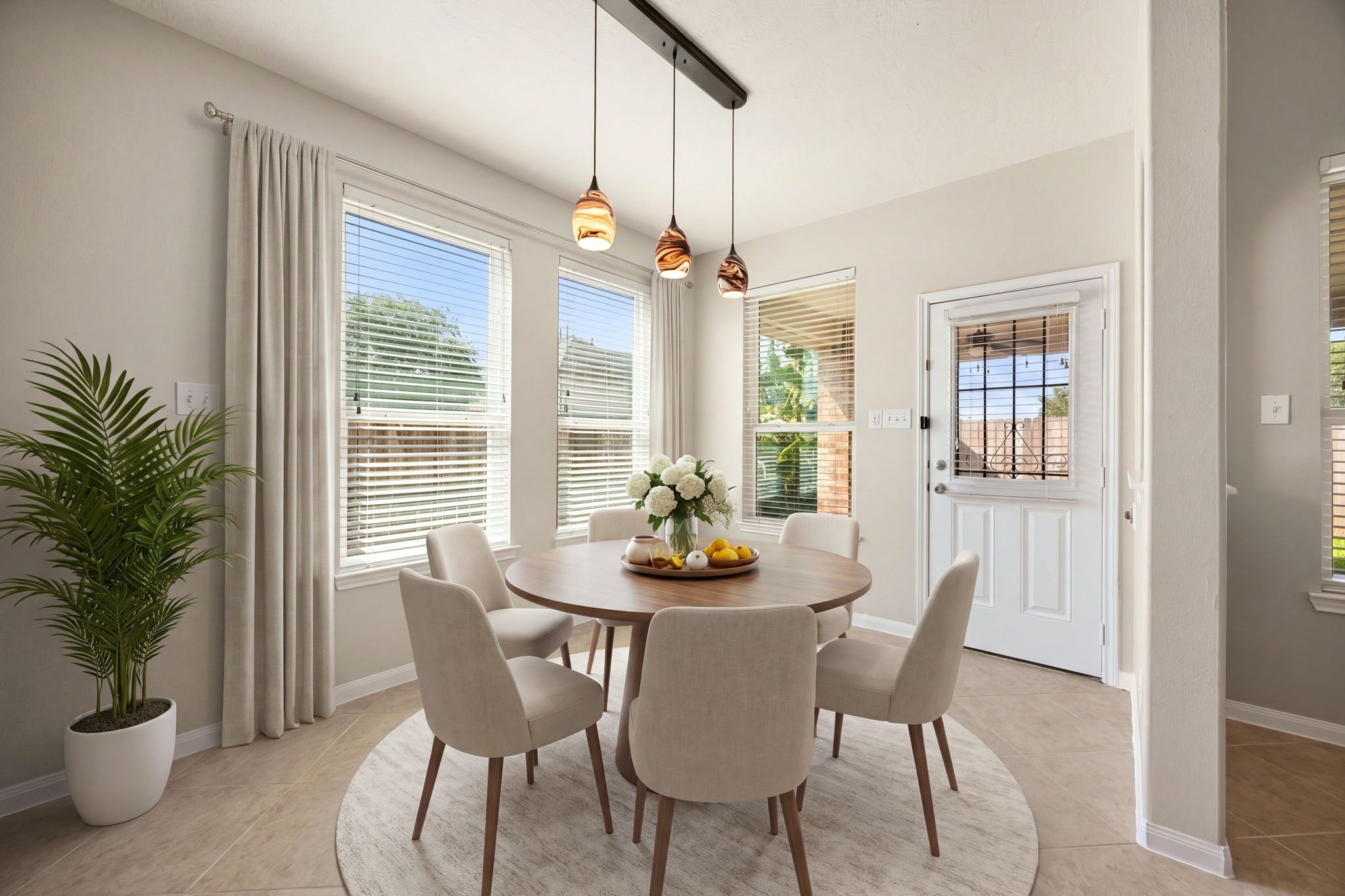 Natural light fills this charming breakfast nook, creating a warm and inviting space for casual daily dining. Tucked just off the kitchen, the area features a trio of multi-tonal glass pendant lights, a wall of large windows overlooking the yard, and a half-lite back door that provides convenient, direct access to the outdoor patio. *Virtually Staged