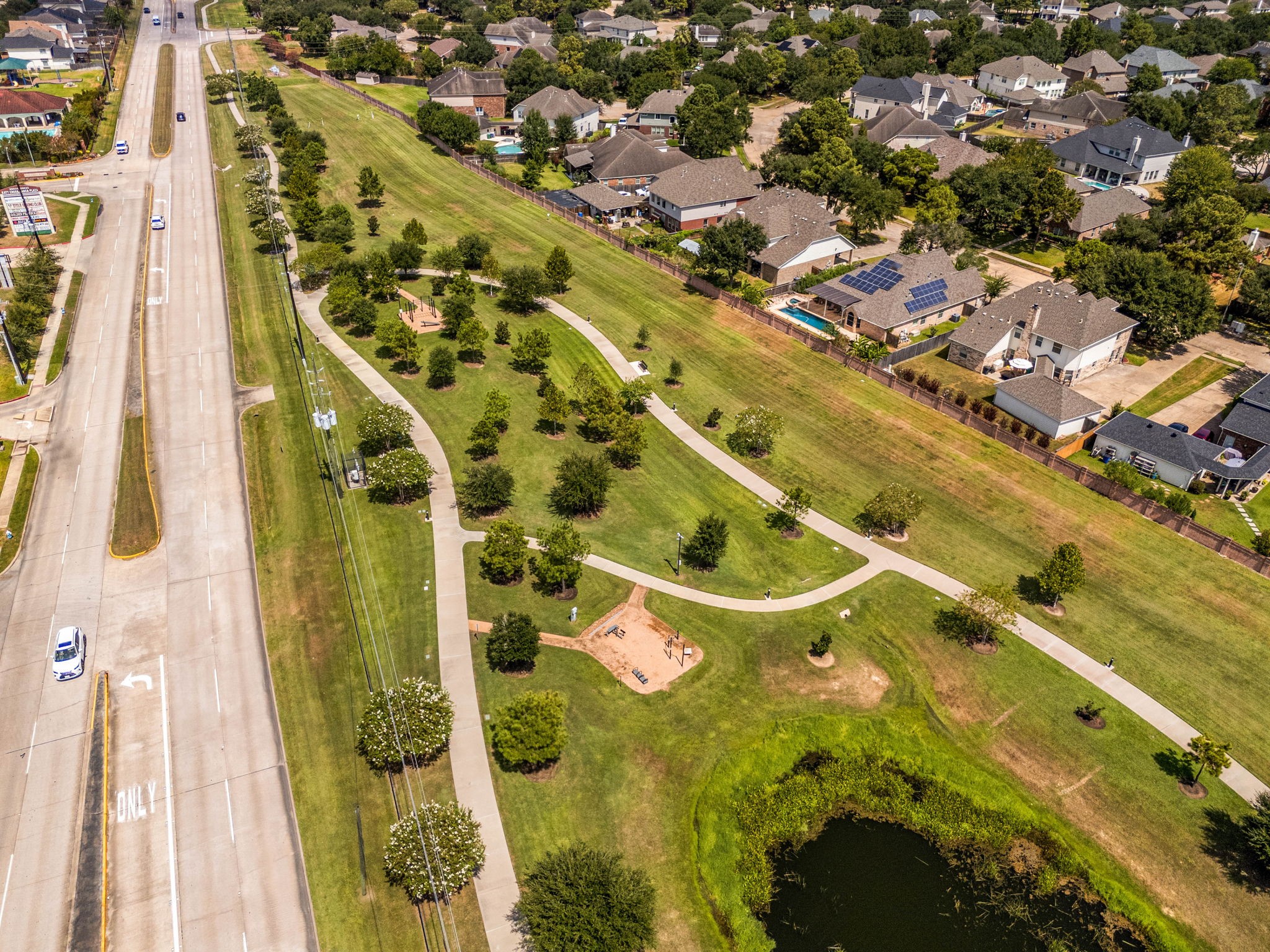 Enjoy miles of scenic exploration right outside your door with this alternative view of the community's extensive greenbelt system. The aerial perspective highlights the network of wide, paved walking and jogging trails that meander through beautifully landscaped fields, passing by a secondary playground station, shaded rest benches, and a peaceful water feature.