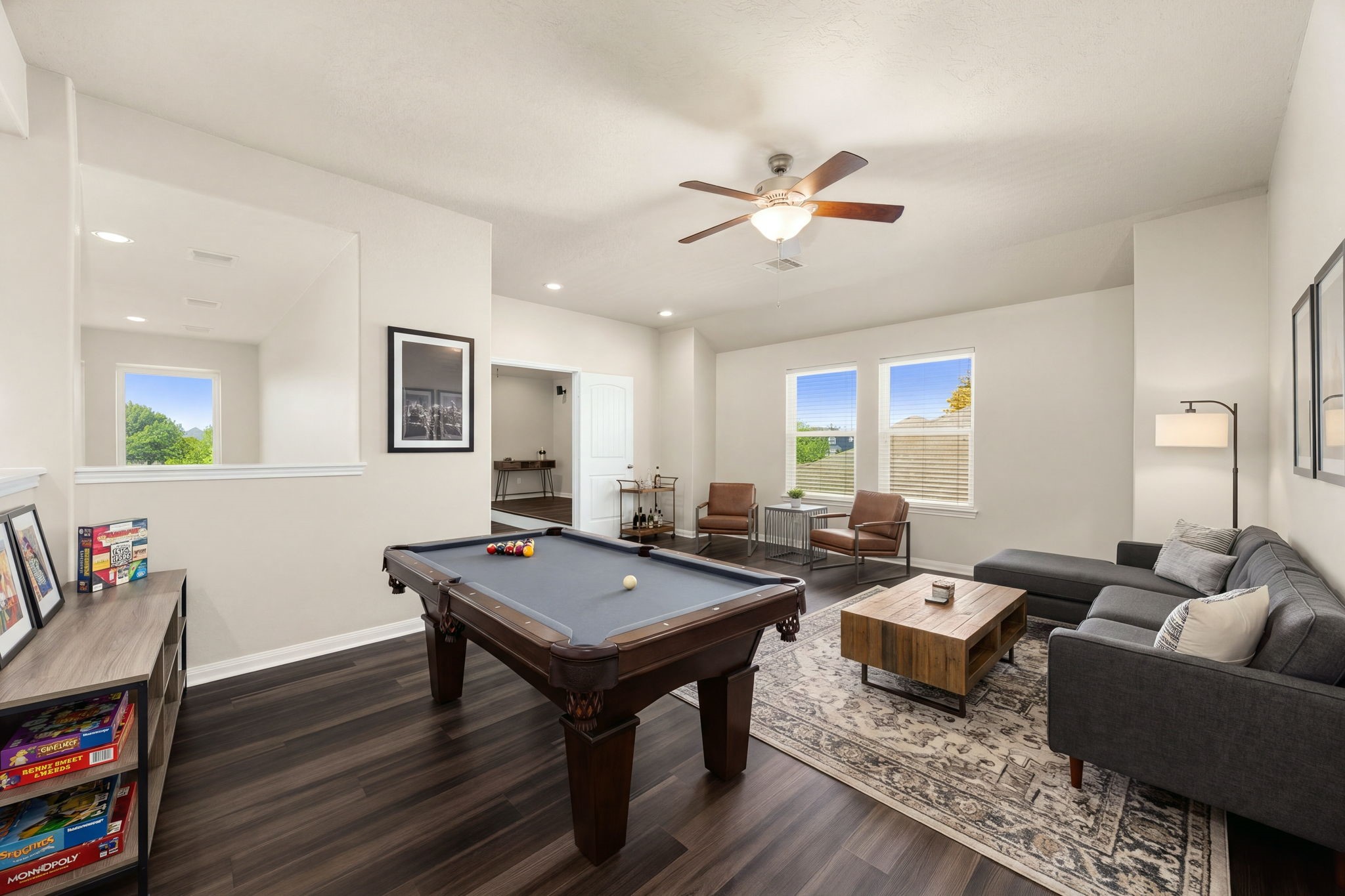 This massive upstairs game room offers endless possibilities for entertainment, recreation, or a quiet study loung. The sprawling space features rich dark flooring, a modern ceiling fan, and multiple large windows that keep the area bright and open, while a half-wall cutout provides a visual connection to the grand staircase and lower-level living areas. *Virtually Staged