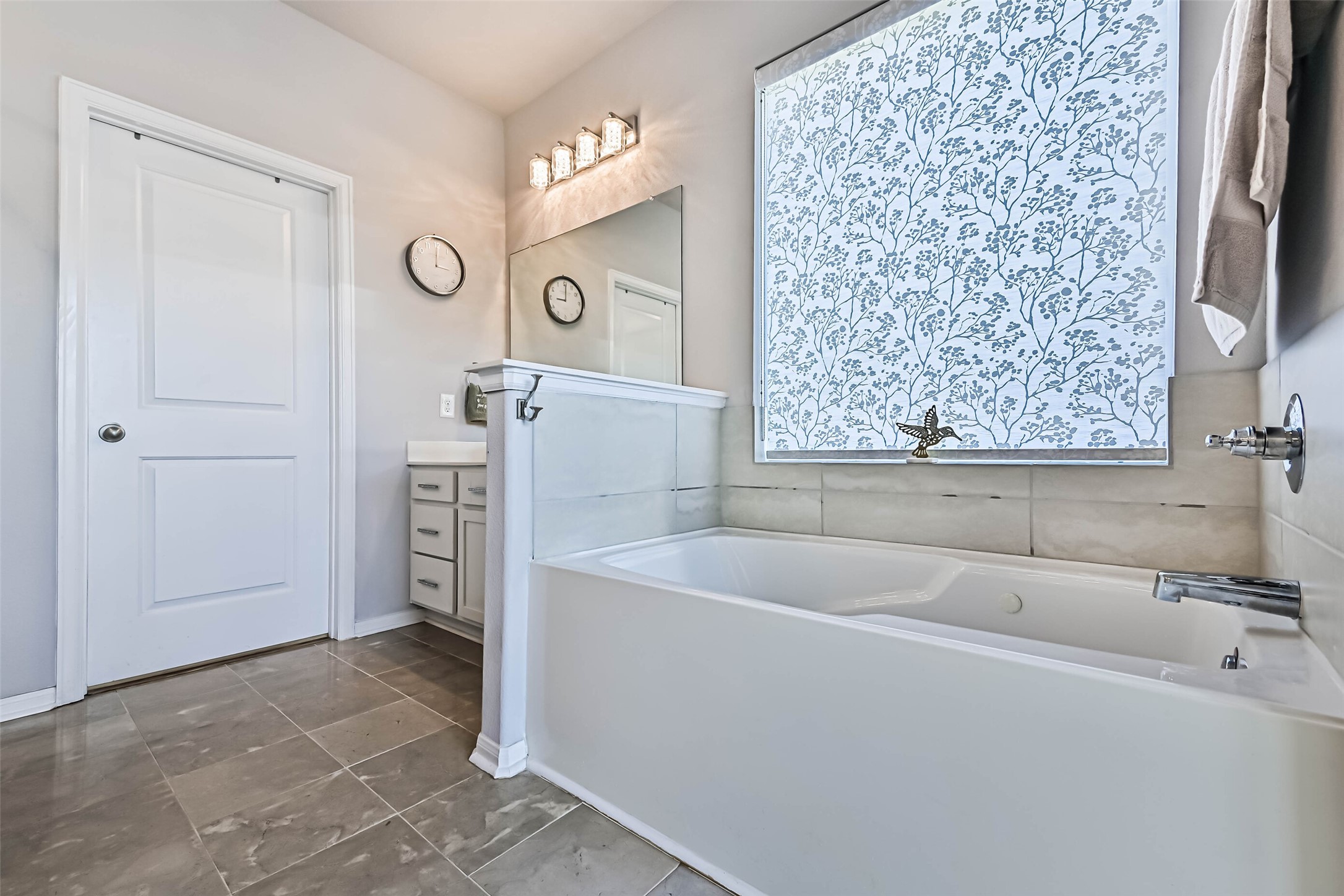 Relaxing soaking tub with tile surround, natural light, and a decorative window shade for added privacy.