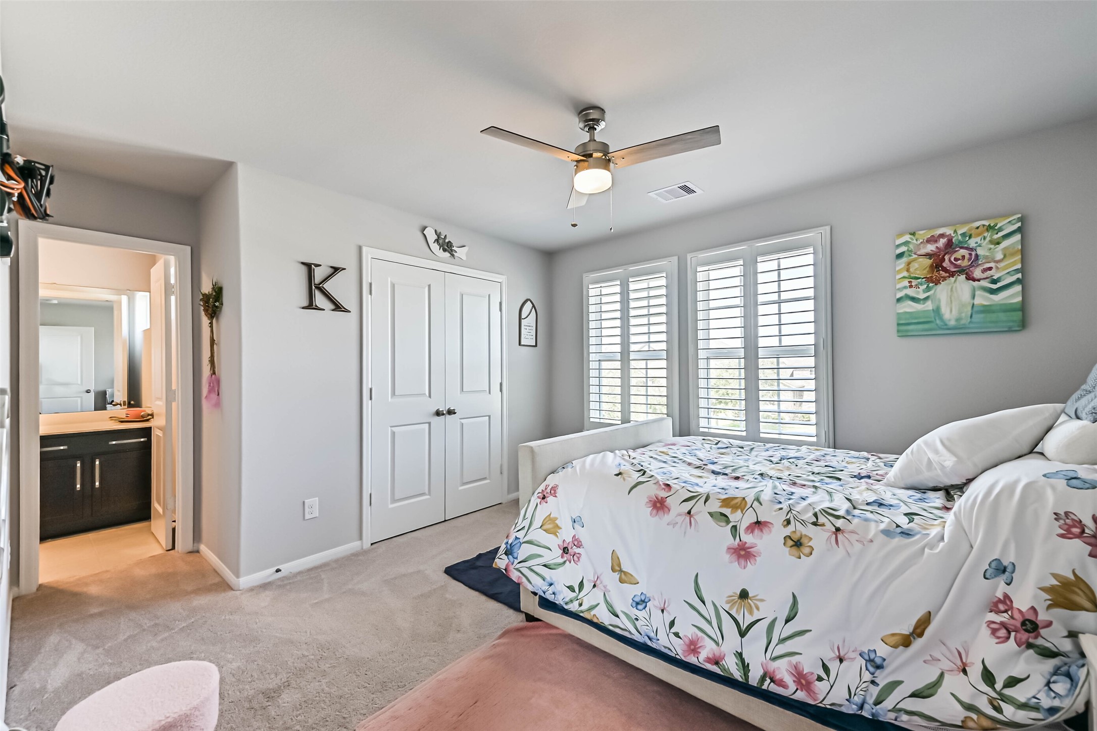 Comfortable bedroom featuring natural light, plantation shutters, ceiling fan, and convenient bathroom access.