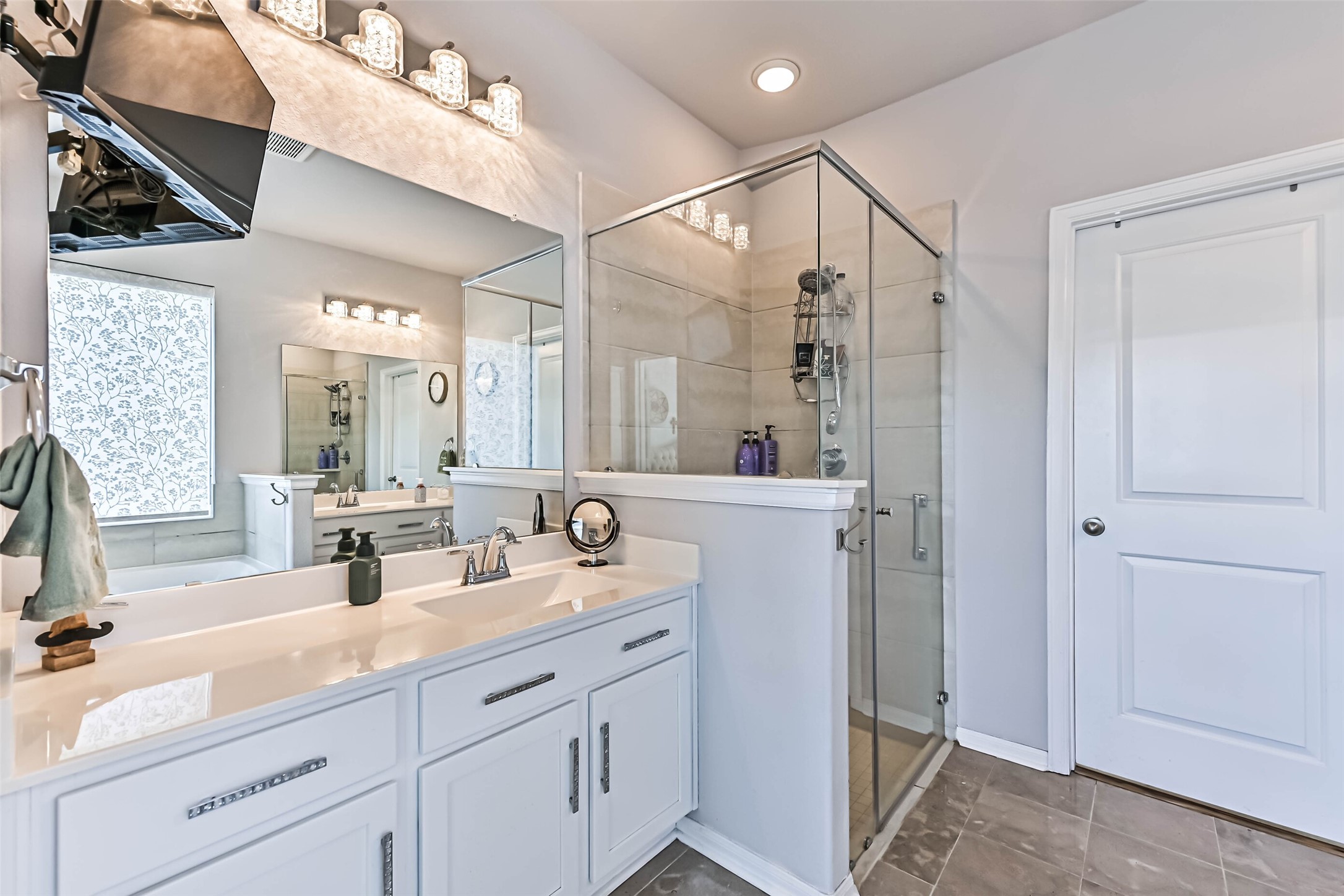 Spacious primary bathroom featuring a long vanity, oversized mirror, modern lighting, and a separate glass-enclosed shower.