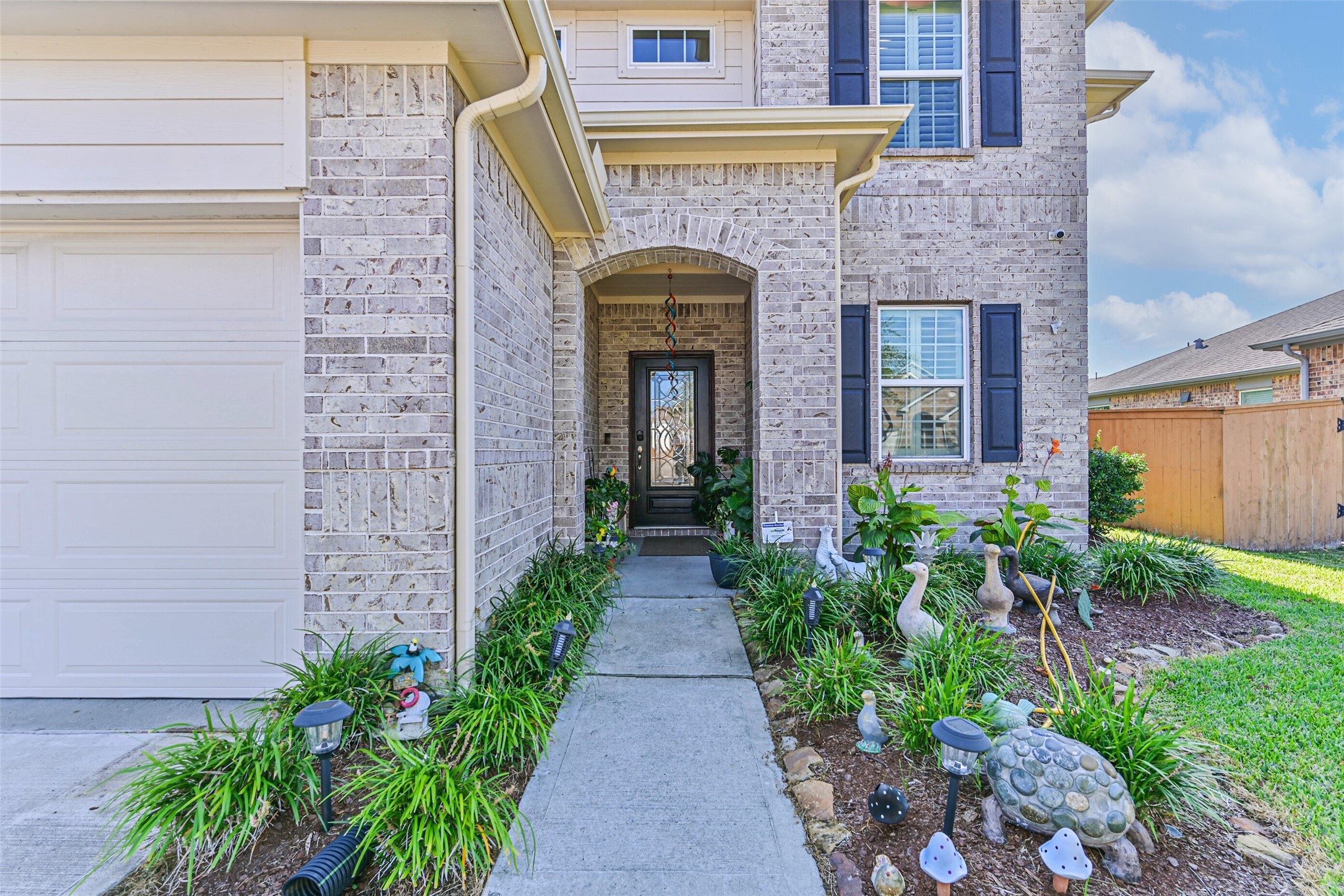 Inviting covered front entrance featuring an arched brick entry, decorative glass front door, and landscaped walkway.
