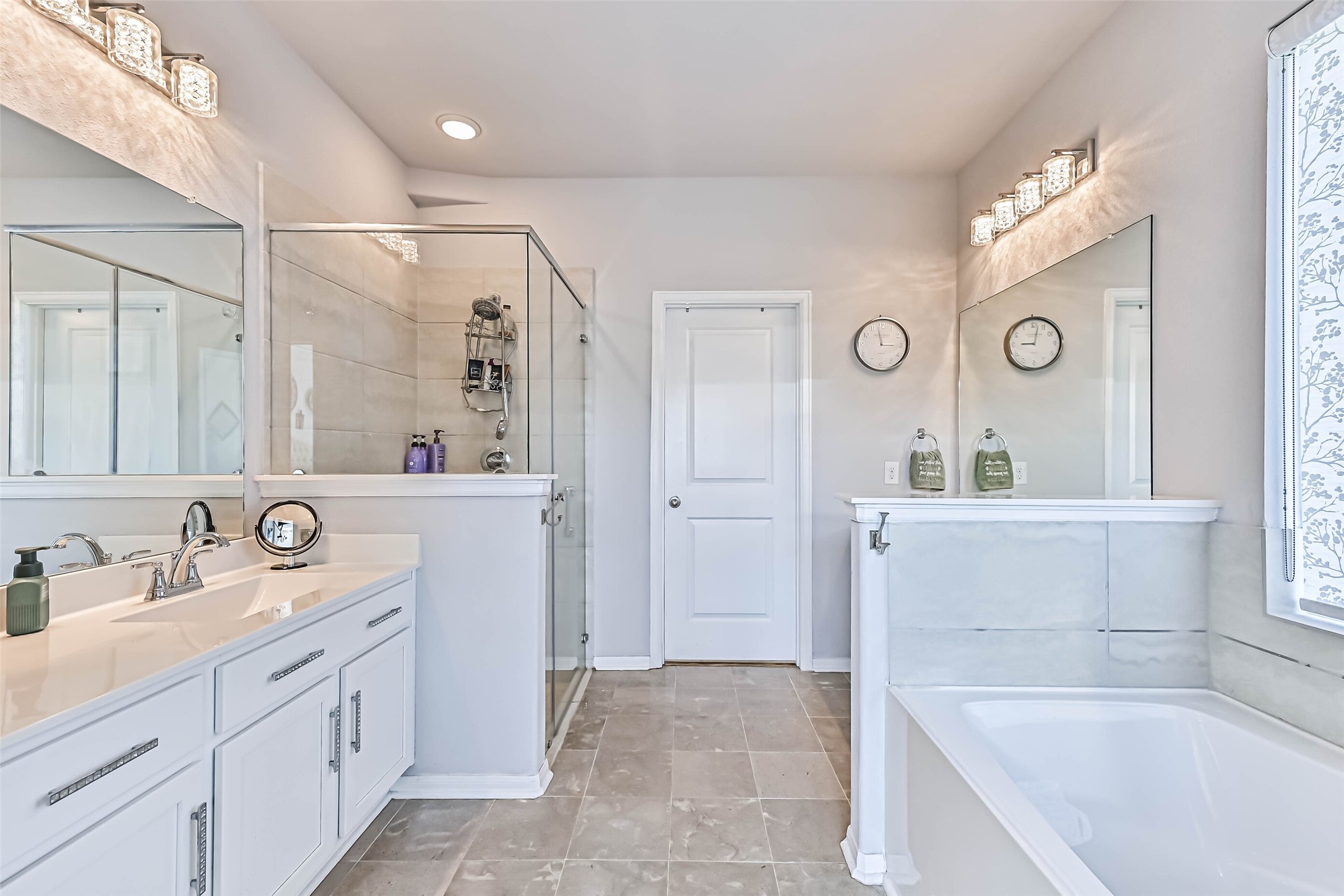 Wide-angle view of the primary bathroom showcasing the separate soaking tub and glass-enclosed shower, spacious vanity, and tile flooring.