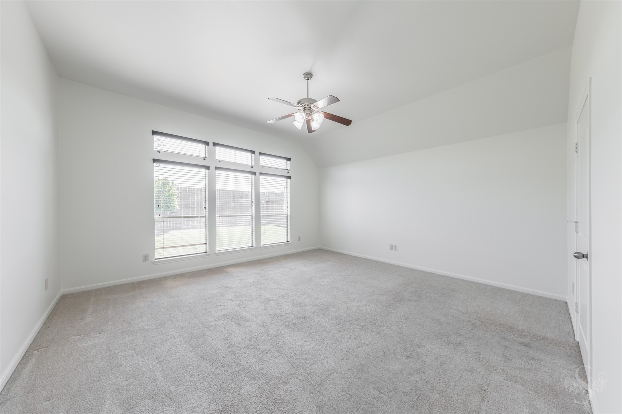 The spacious primary suite offers a peaceful retreat with elevated ceilings and soft natural light from the wall of windows. The generous layout provides plenty of room for a sitting area by the windows, creating the perfect spot to relax with a book or morning coffee.