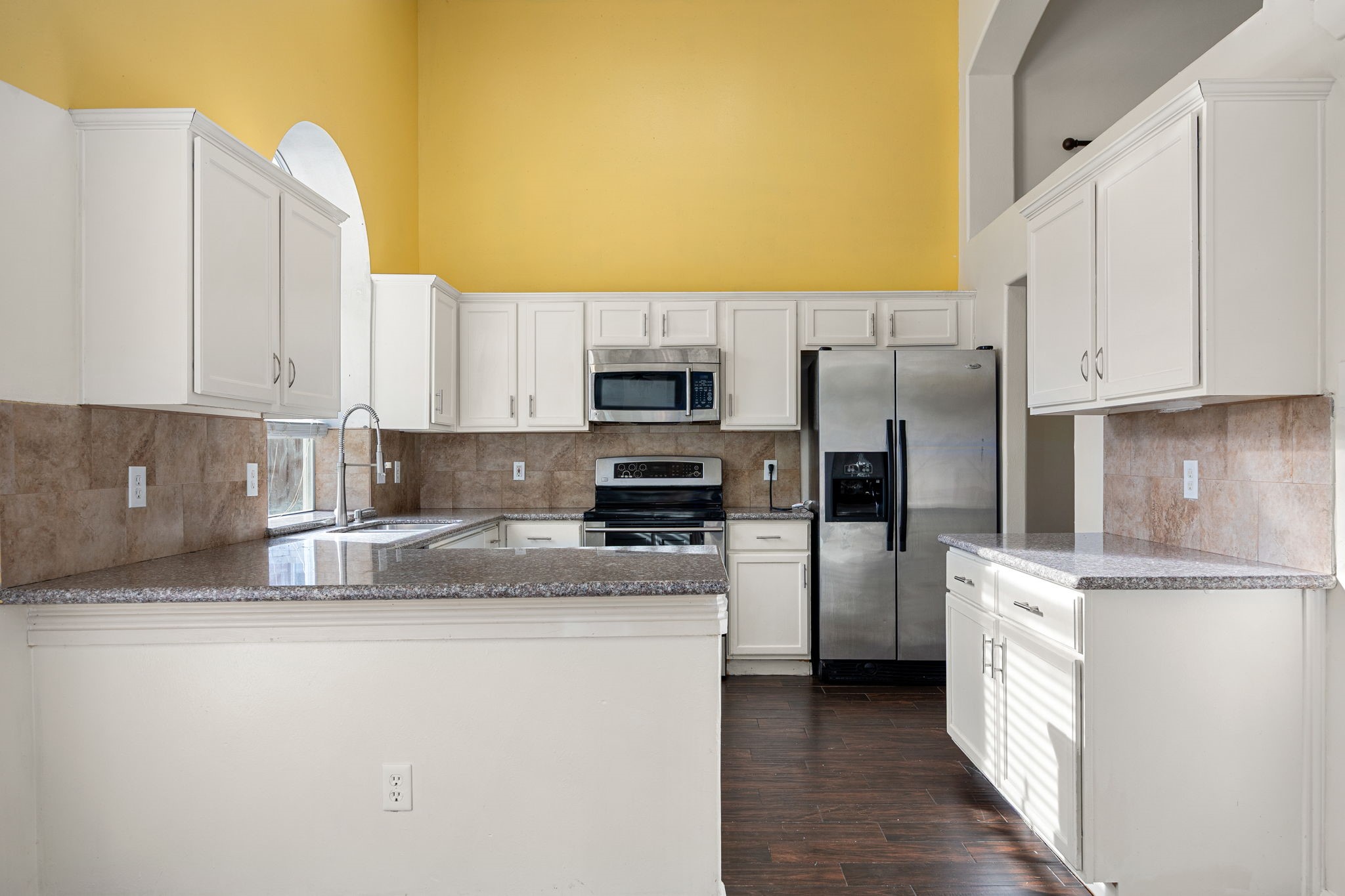 Crisp white cabinetry and breakfast bar seating complete this well-equipped kitchen, perfect for quick meals or casual entertaining.
