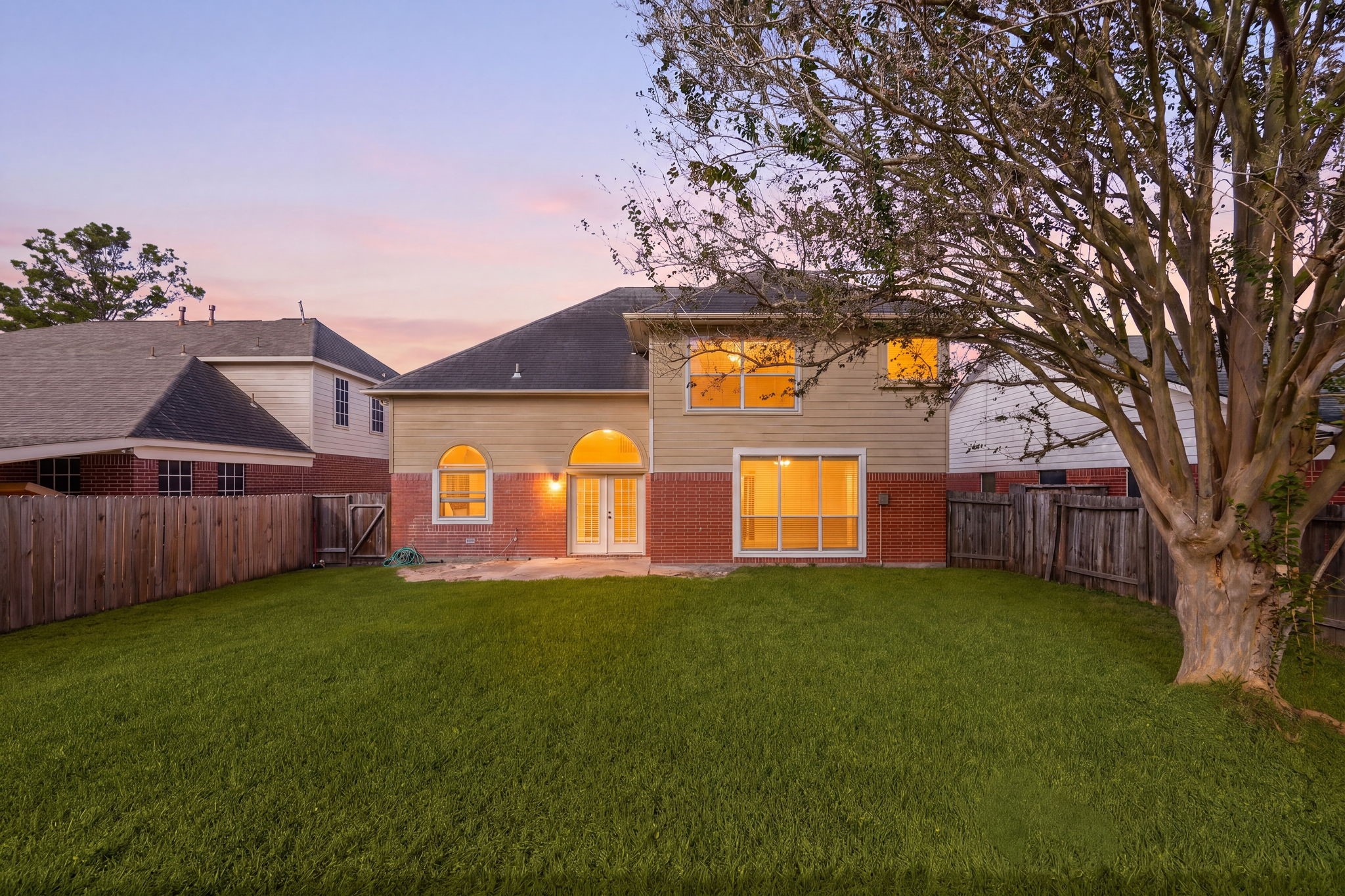 As evening falls, the spacious backyard glows beautifully, framed by mature trees and plenty of room to relax or entertain.