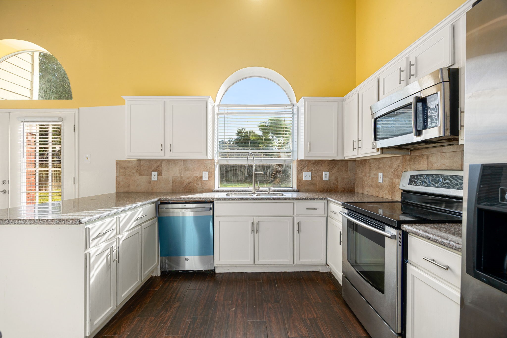 The bright kitchen features granite countertops, a tile backsplash, and stainless steel appliances, with a large window overlooking the backyard.