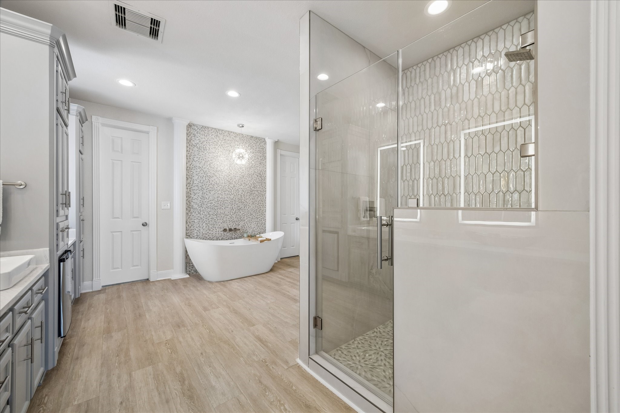 Relax and unwind in the elegant soaking tub, framed by a striking tiled accent wall. The light and airy finishes create a serene retreat within the completely remodeled primary bathroom. Remodel includes: a new shower, bathtub, sinks, faucets, flooring, mirrors, towel bars, beverage refrigerator & lighting.