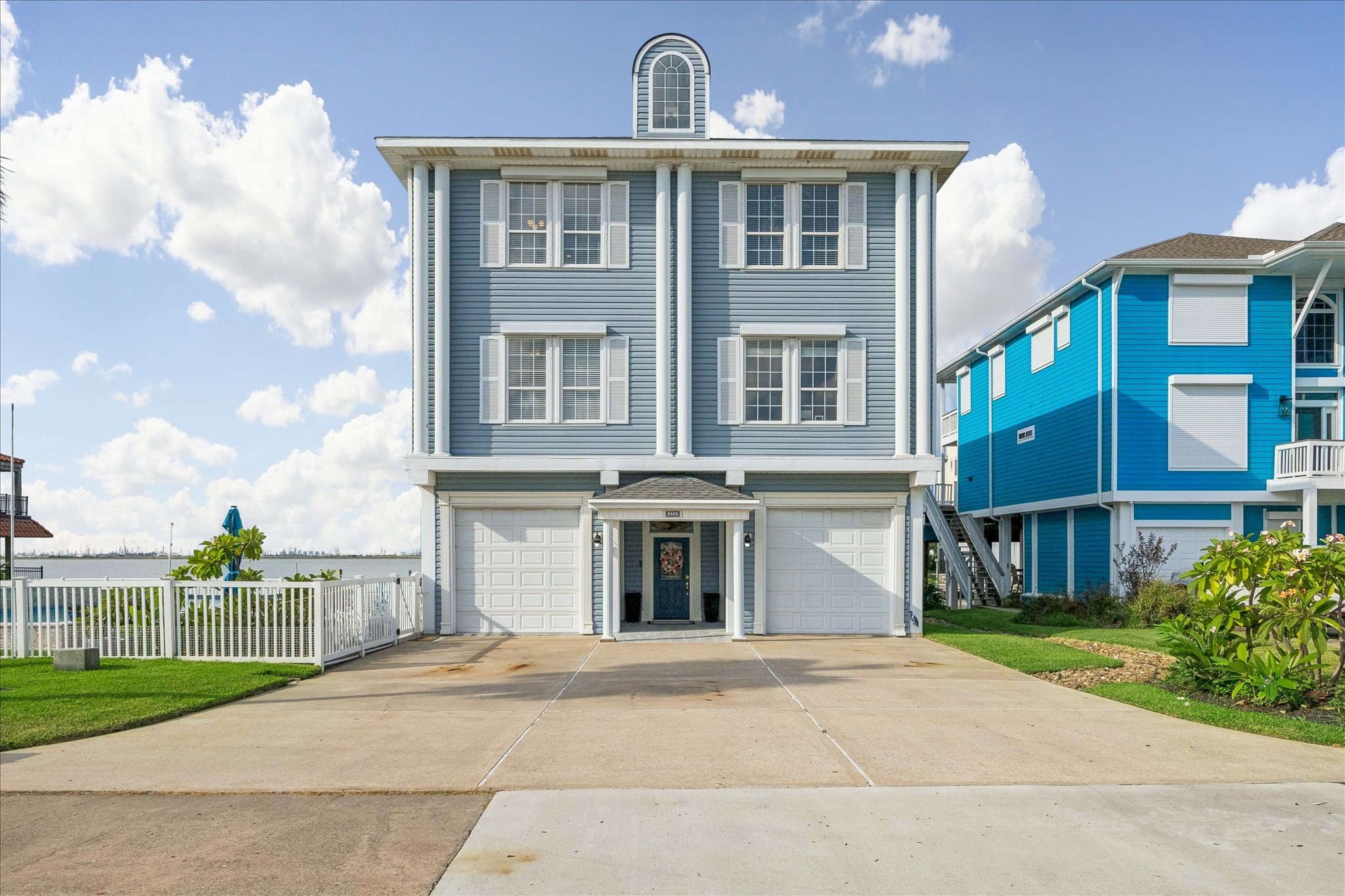 Charming coastal home featuring a classic blue exterior with white trim, spacious three-story design, New tile flooring in outdoor entryway all set against a serene waterfront backdrop.