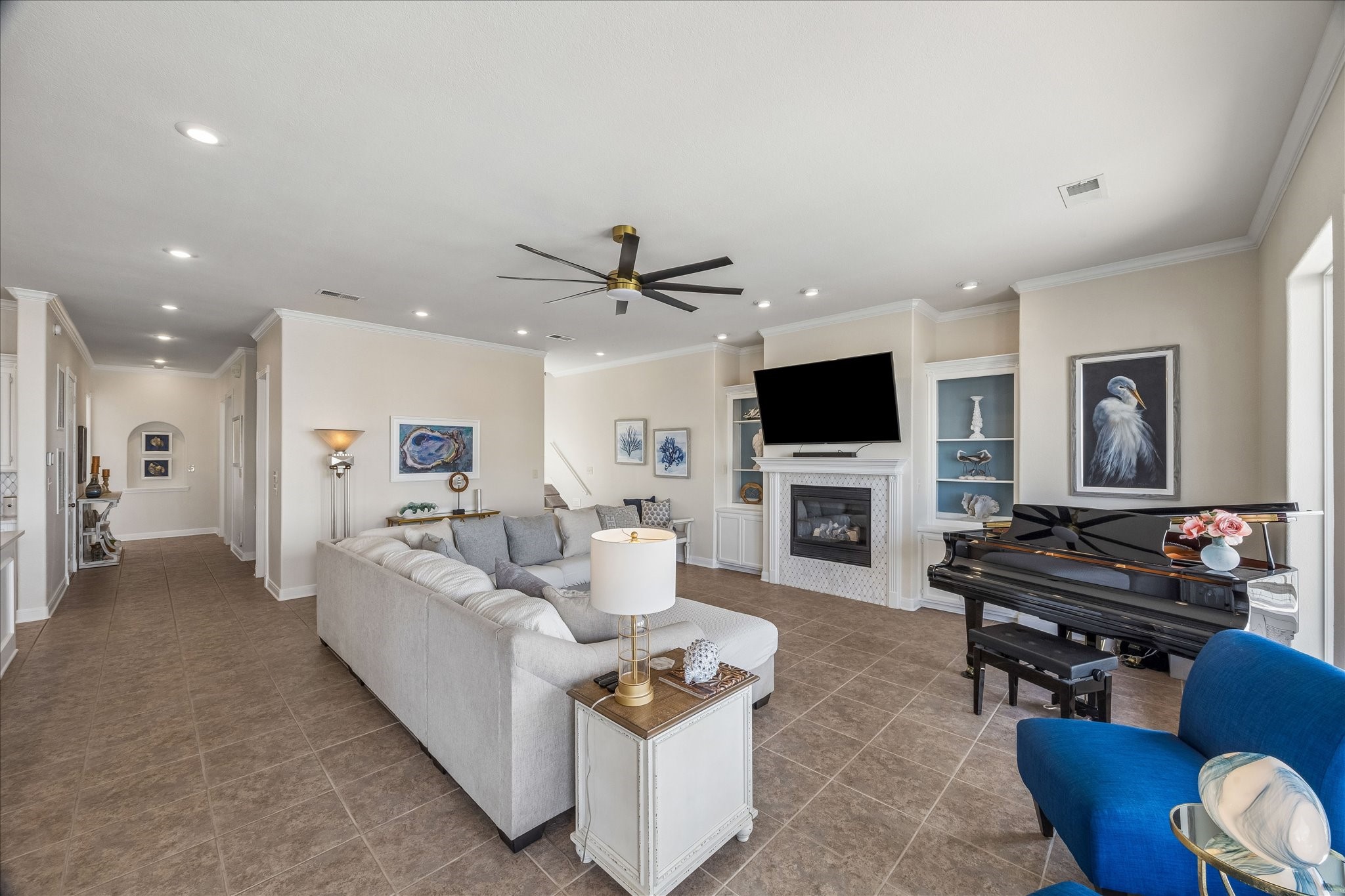 Open-concept living room with tiled flooring, crown molding, fireplace with metal surround updated with new trim & quartz, custom built-ins and abundant storage.