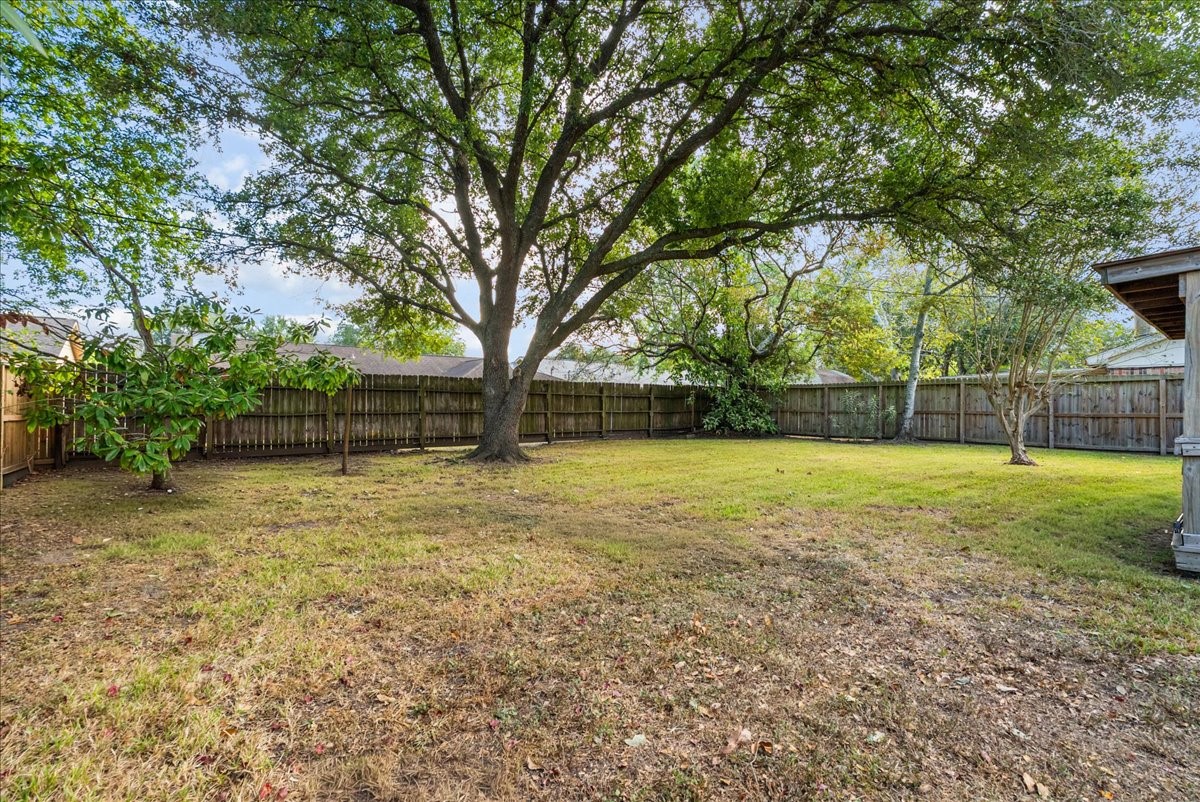 Fenced backyard with mature shade trees and open lawn space for outdoor enjoyment.