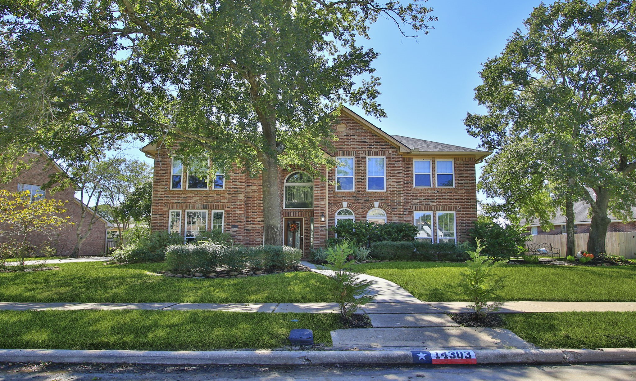 Stately two-story brick home set amidst lush greenery and mature trees, featuring a charming pathway leading to an elegant arched entryway.