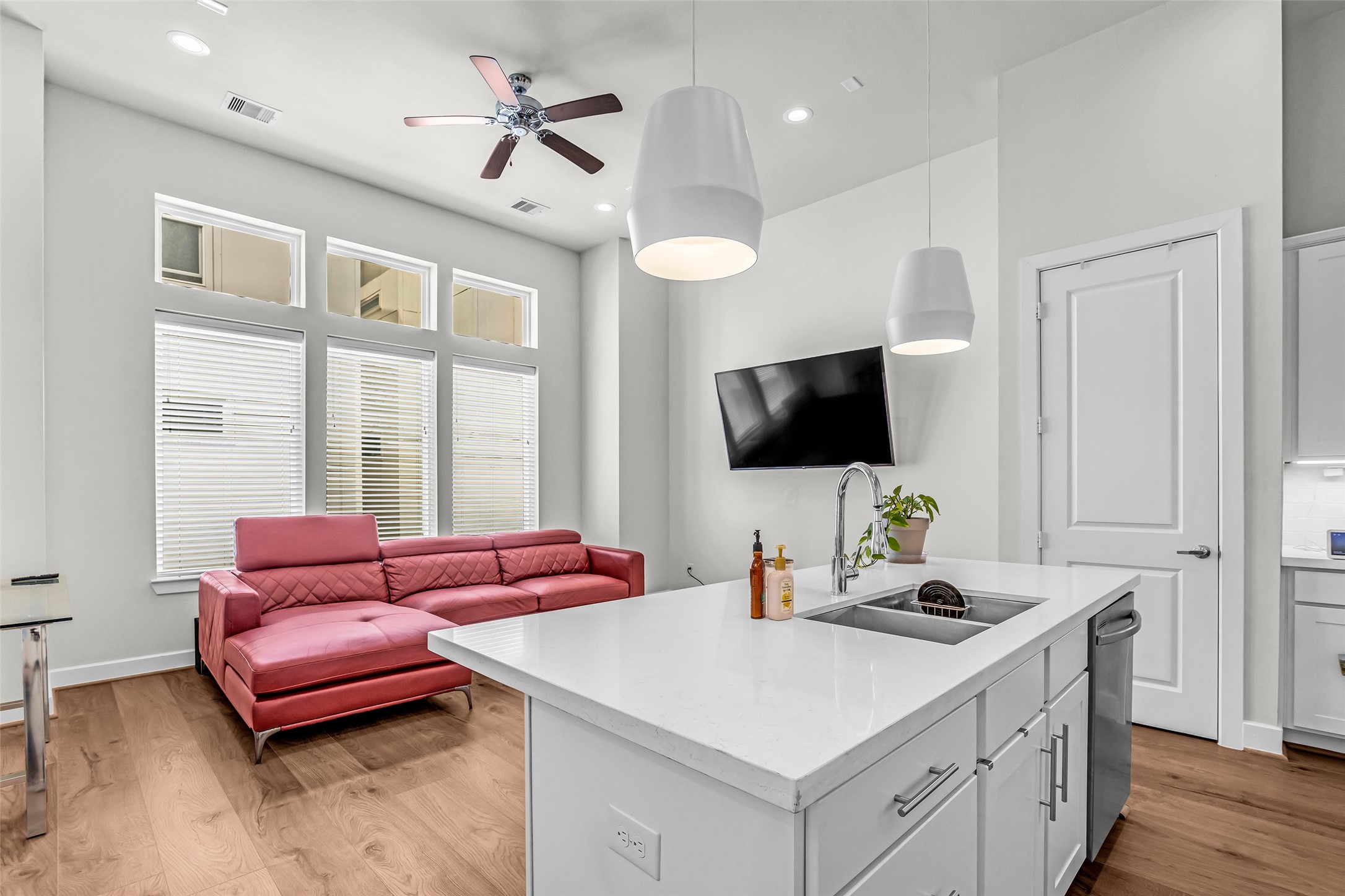 The kitchen, dining area, and living room are filled with natural light coming through large windows along the living room wall, creating a bright and welcoming shared space.